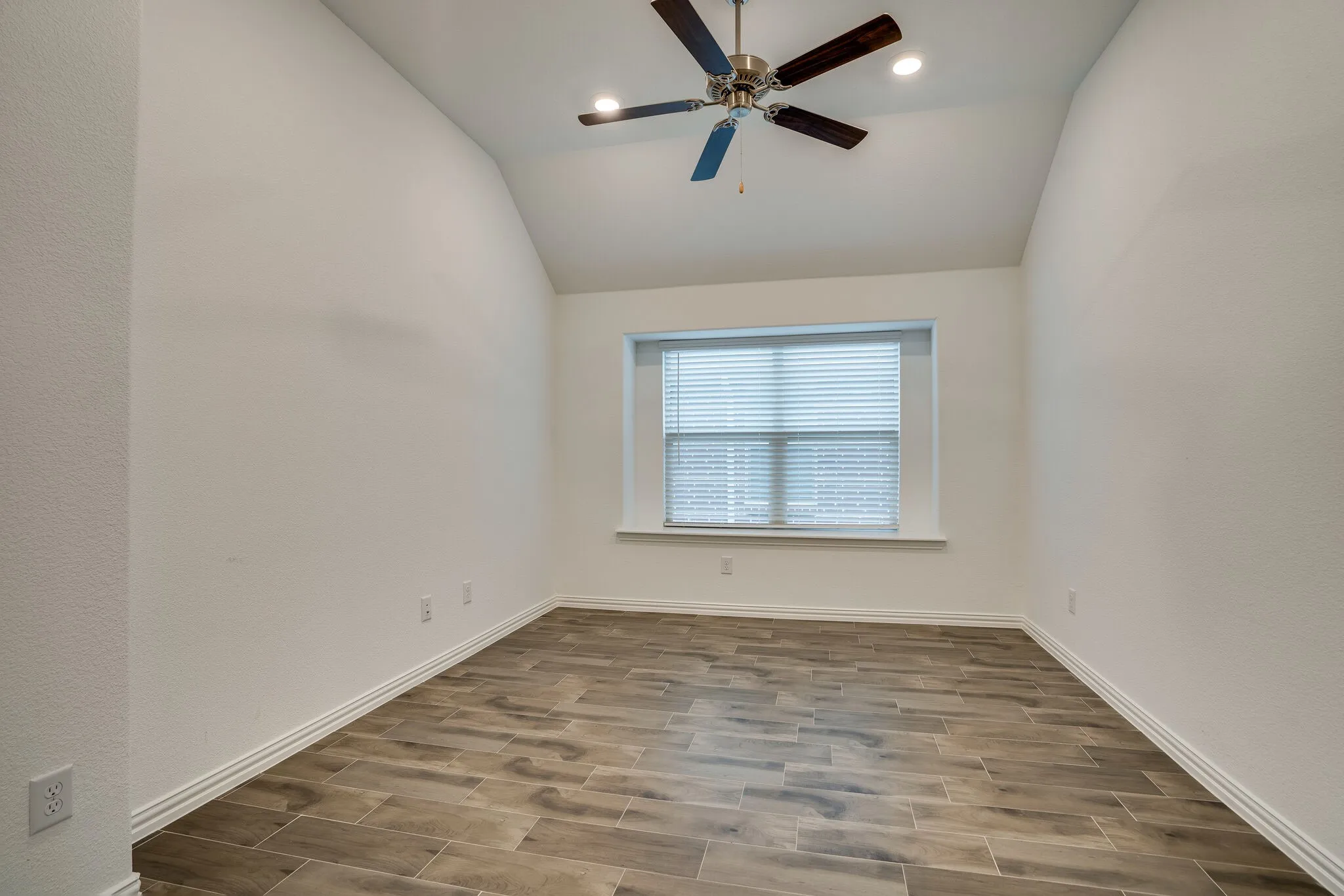 Room featuring wood-finish tile flooring, vaulted ceiling, a ceiling fan with integrated lighting, and a window with horizontal blinds