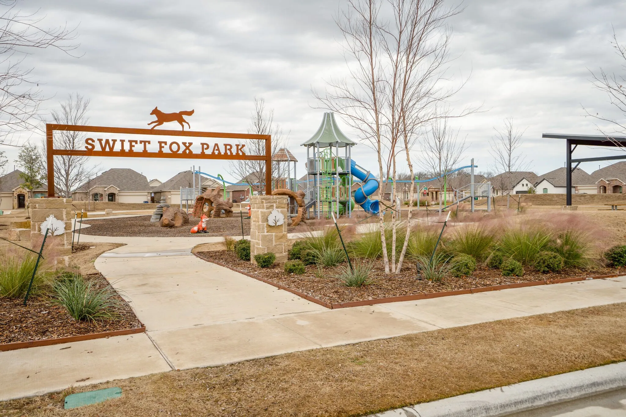 Community park entrance featuring a decorative metal sign, stone pillar accents, and a paved walkway