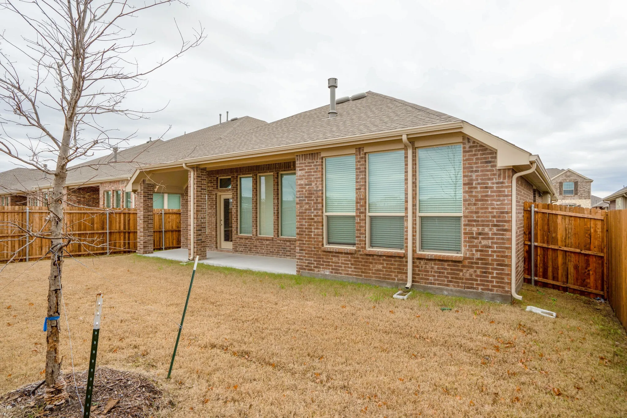 Spacious backyard with a covered patio, brick exterior, multiple windows, and a wood privacy fence