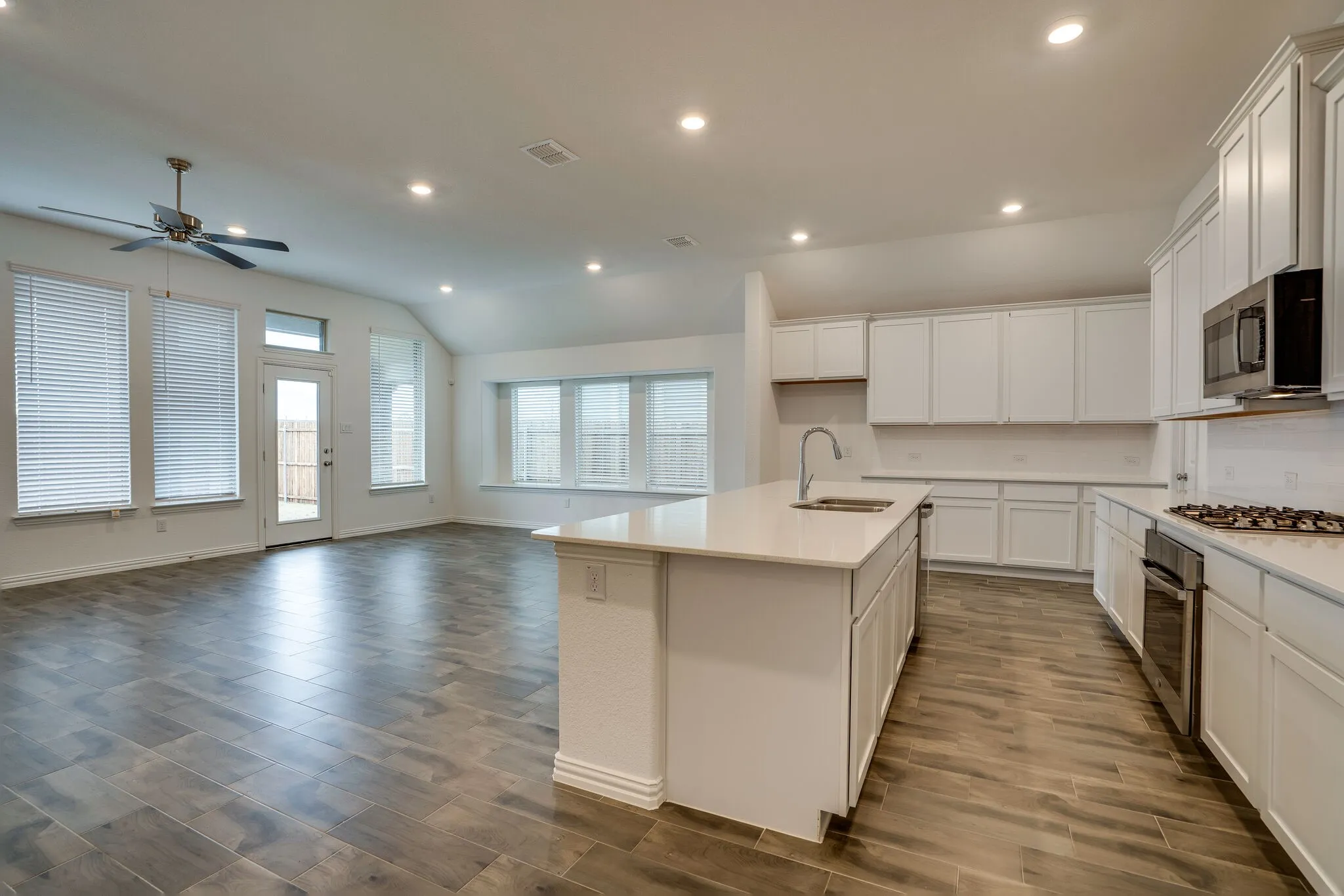Open-concept kitchen and living area featuring wood-finish flooring, recessed lighting, and a vaulted ceiling