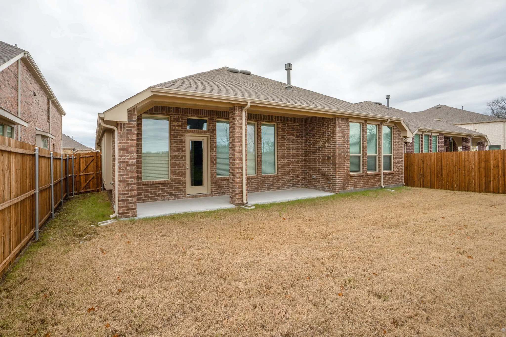 Brick exterior featuring a covered concrete patio and a fenced backyard