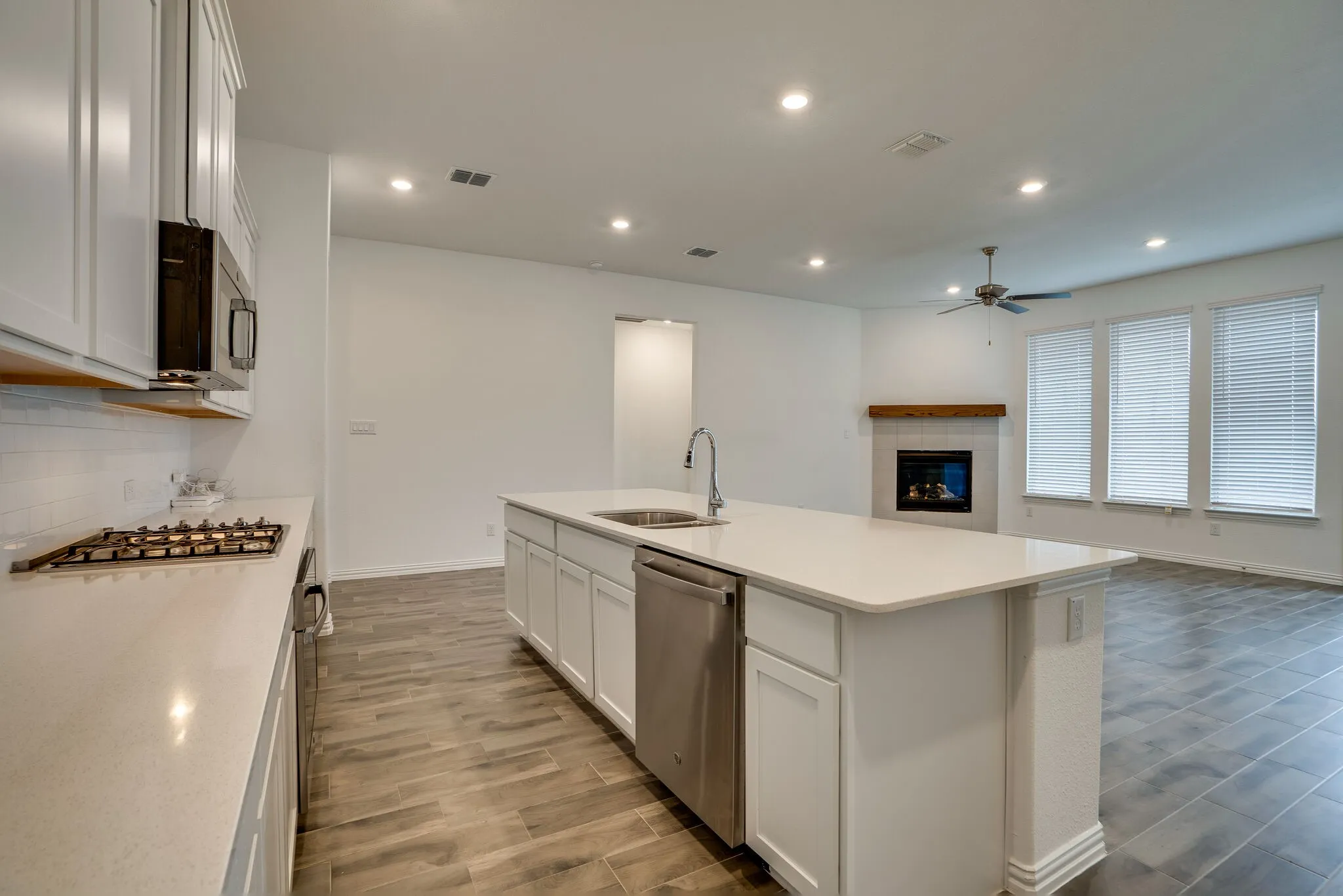 Open concept kitchen featuring an island with an integrated sink and dishwasher, white cabinetry, a gas range, and recessed lighting