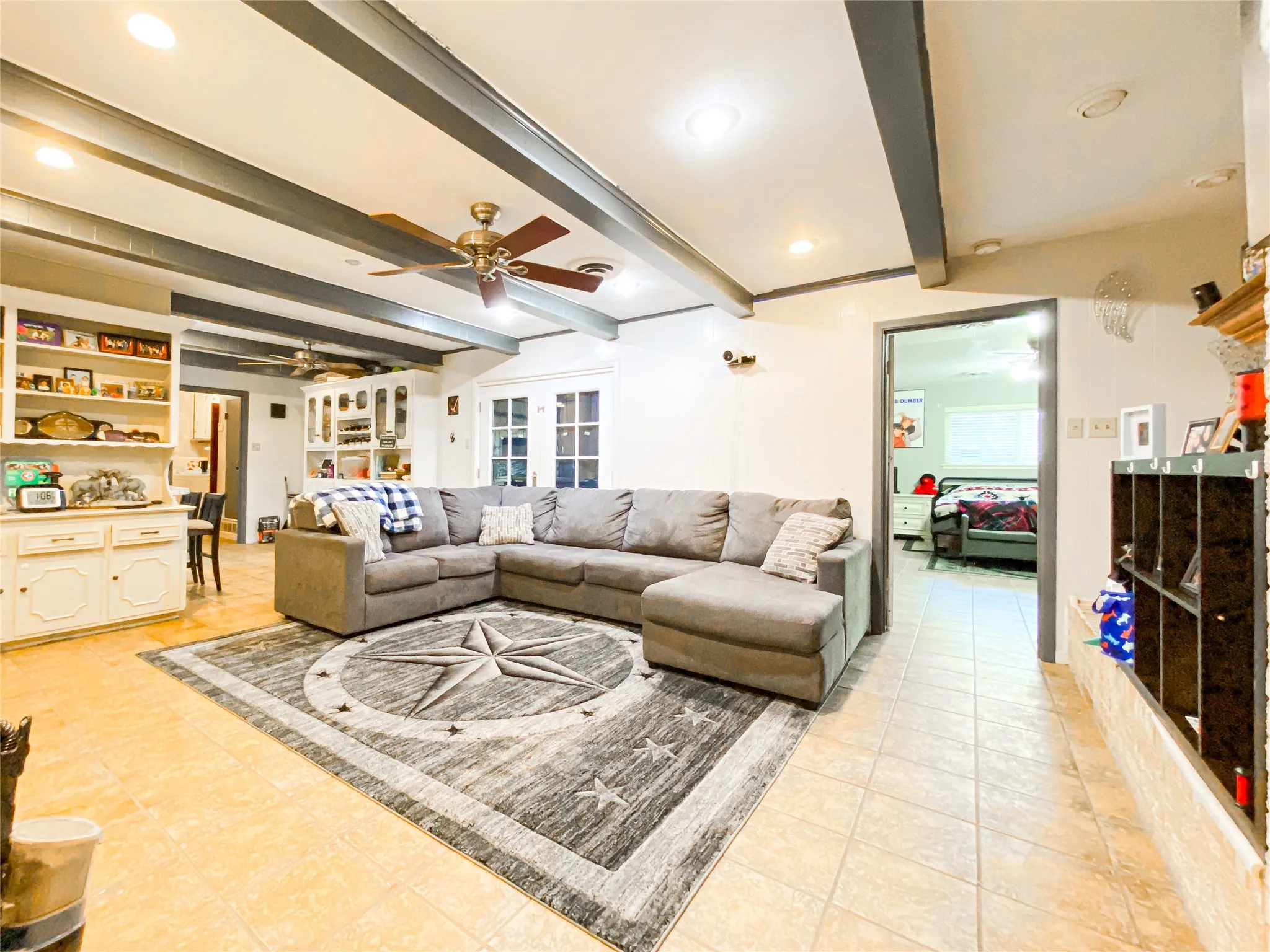 Spacious living area featuring exposed ceiling beams, recessed lighting, and tile flooring