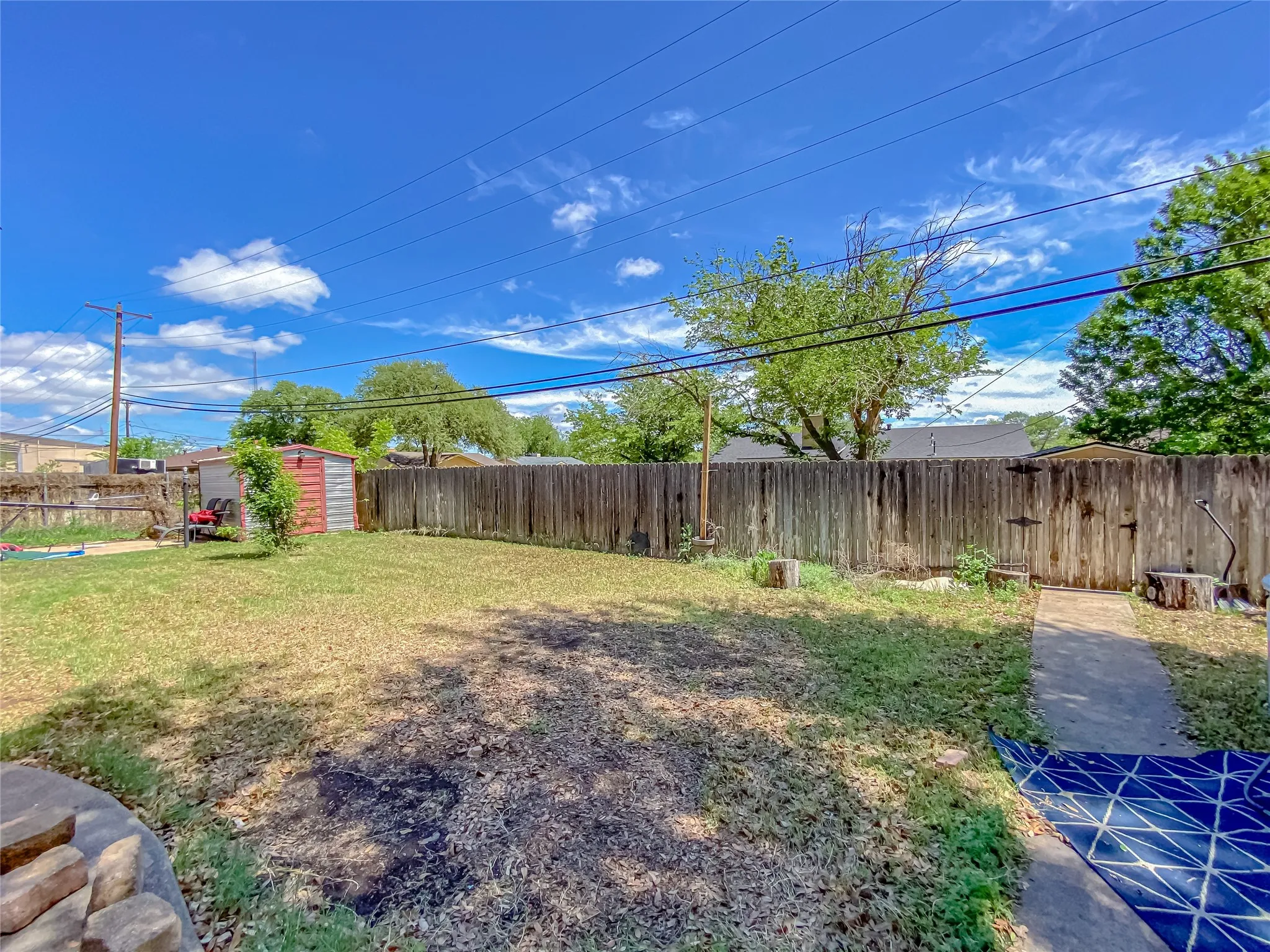 Expansive backyard space featuring a wooden privacy fence, a concrete walkway, and a storage shed