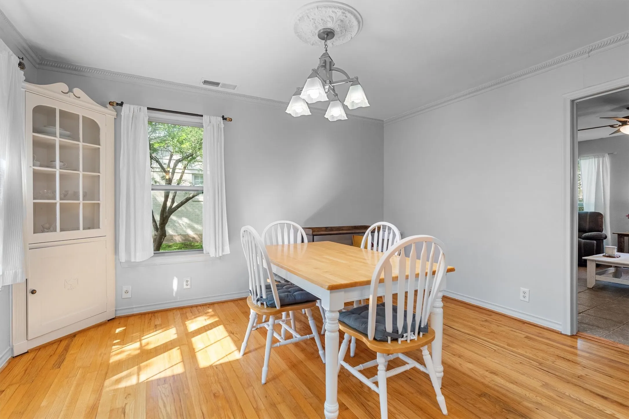 Hardwood flooring throughout, crown molding, and a built-in corner cabinet with glass-front upper doors