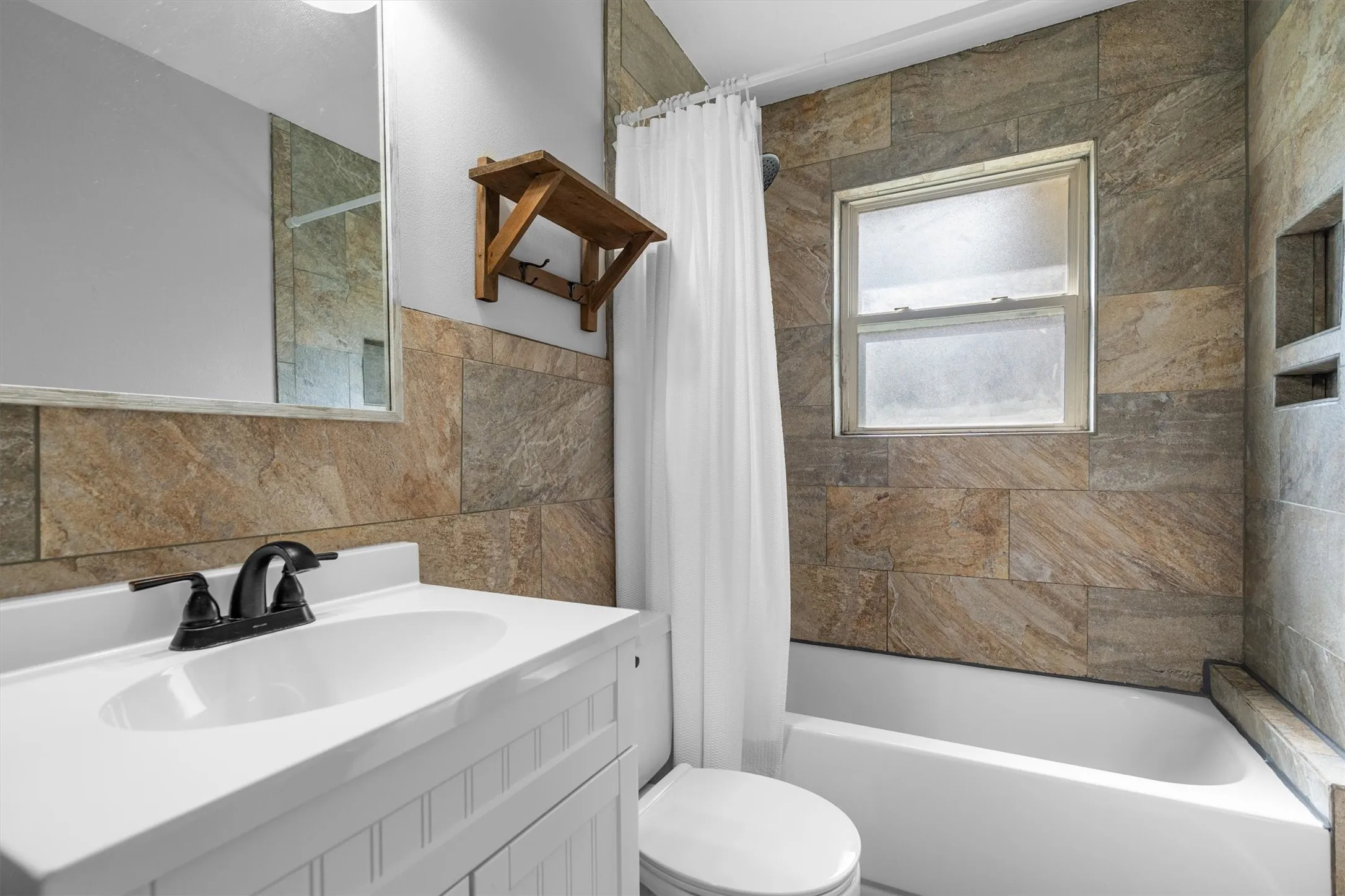 Bathroom featuring a full vanity with a white countertop and sink, dark bronze faucet, tiled walls, and a built-in shower niche