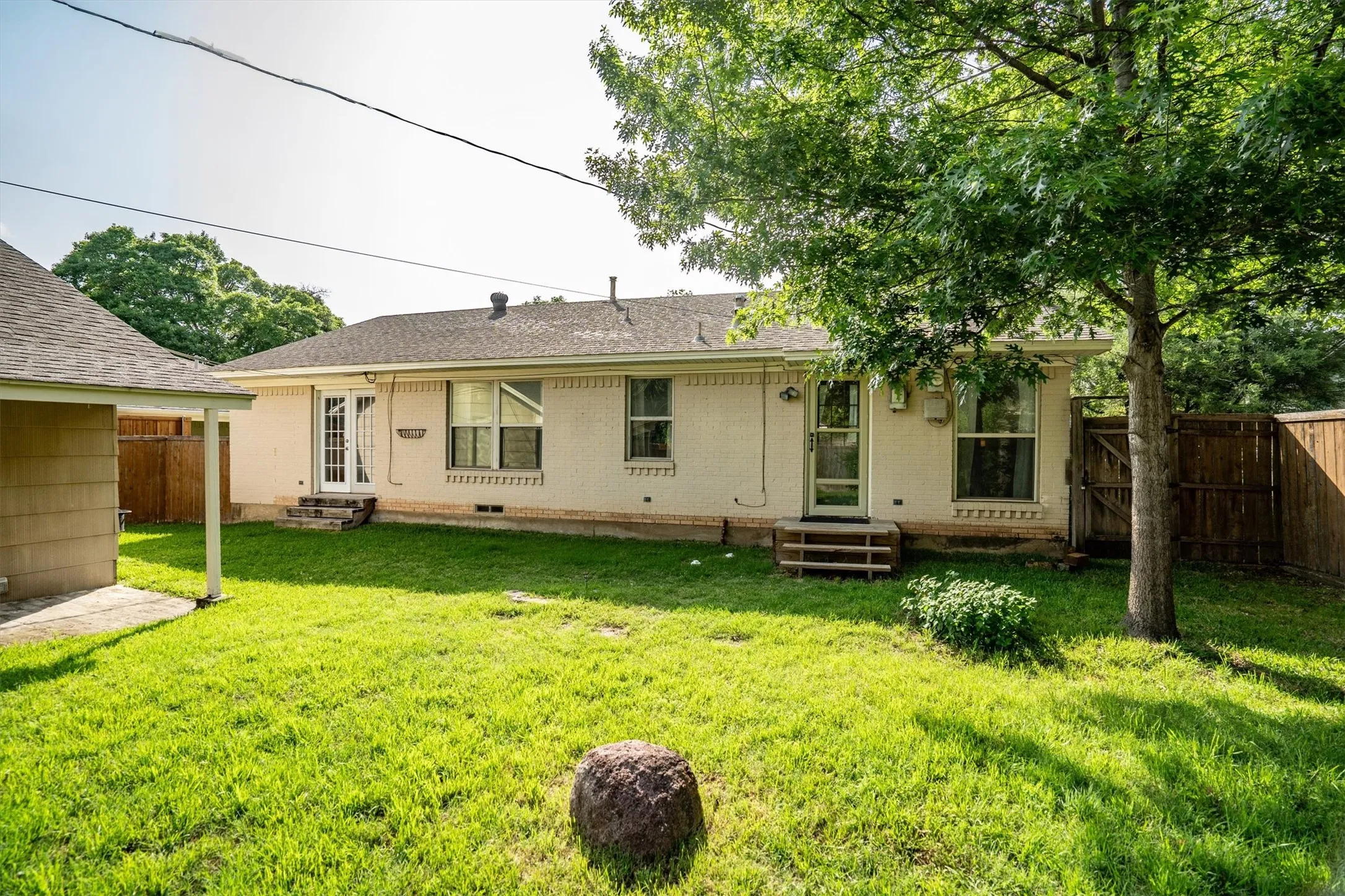 Expansive rear yard featuring a manicured lawn, mature trees, and a privacy fence