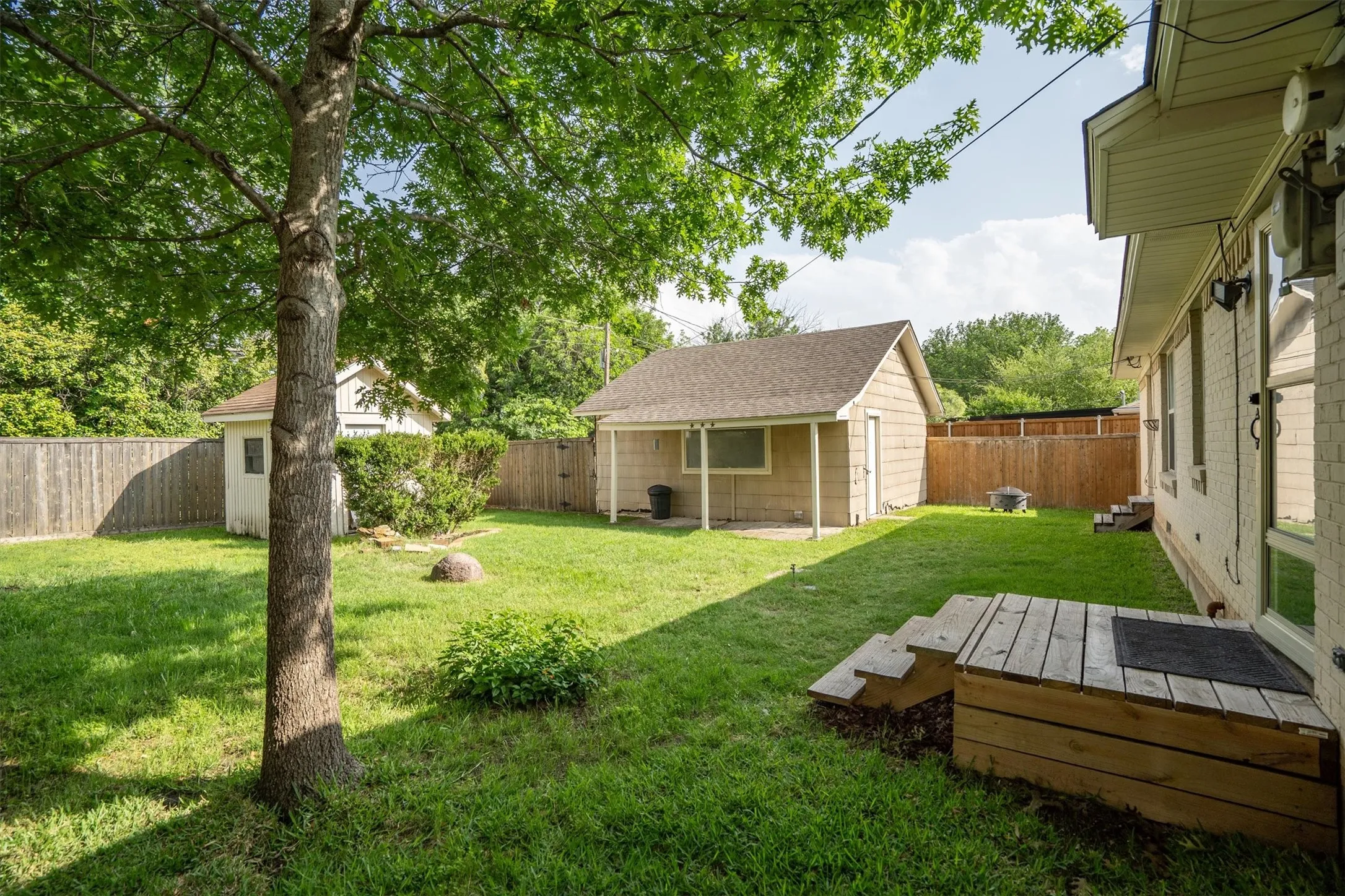 Spacious backyard featuring a detached accessory structure with a covered patio, a separate storage shed, perimeter fencing, and mature trees