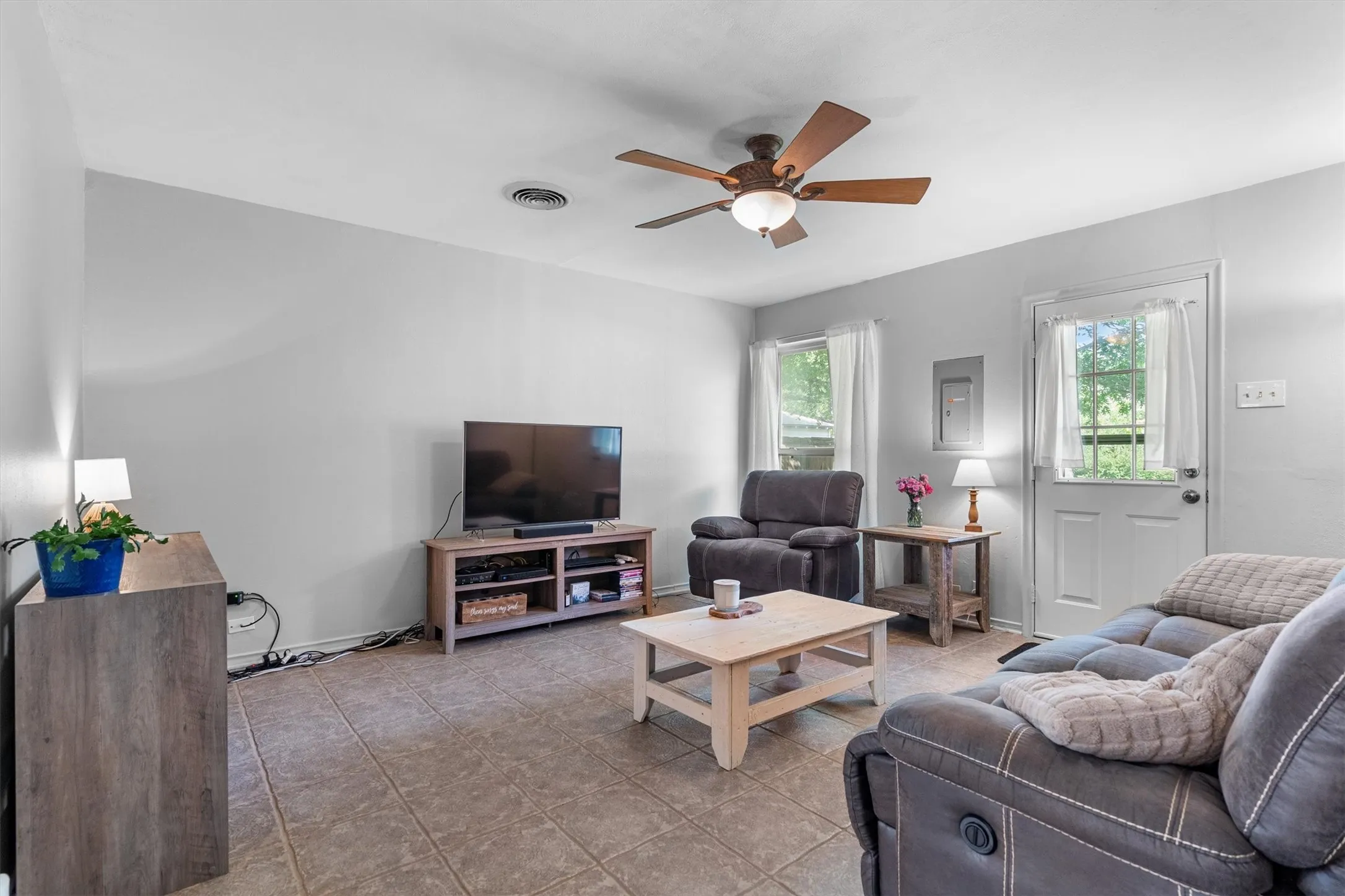 Living area featuring tiled flooring, neutral wall paint, and a ceiling fan with integrated lighting