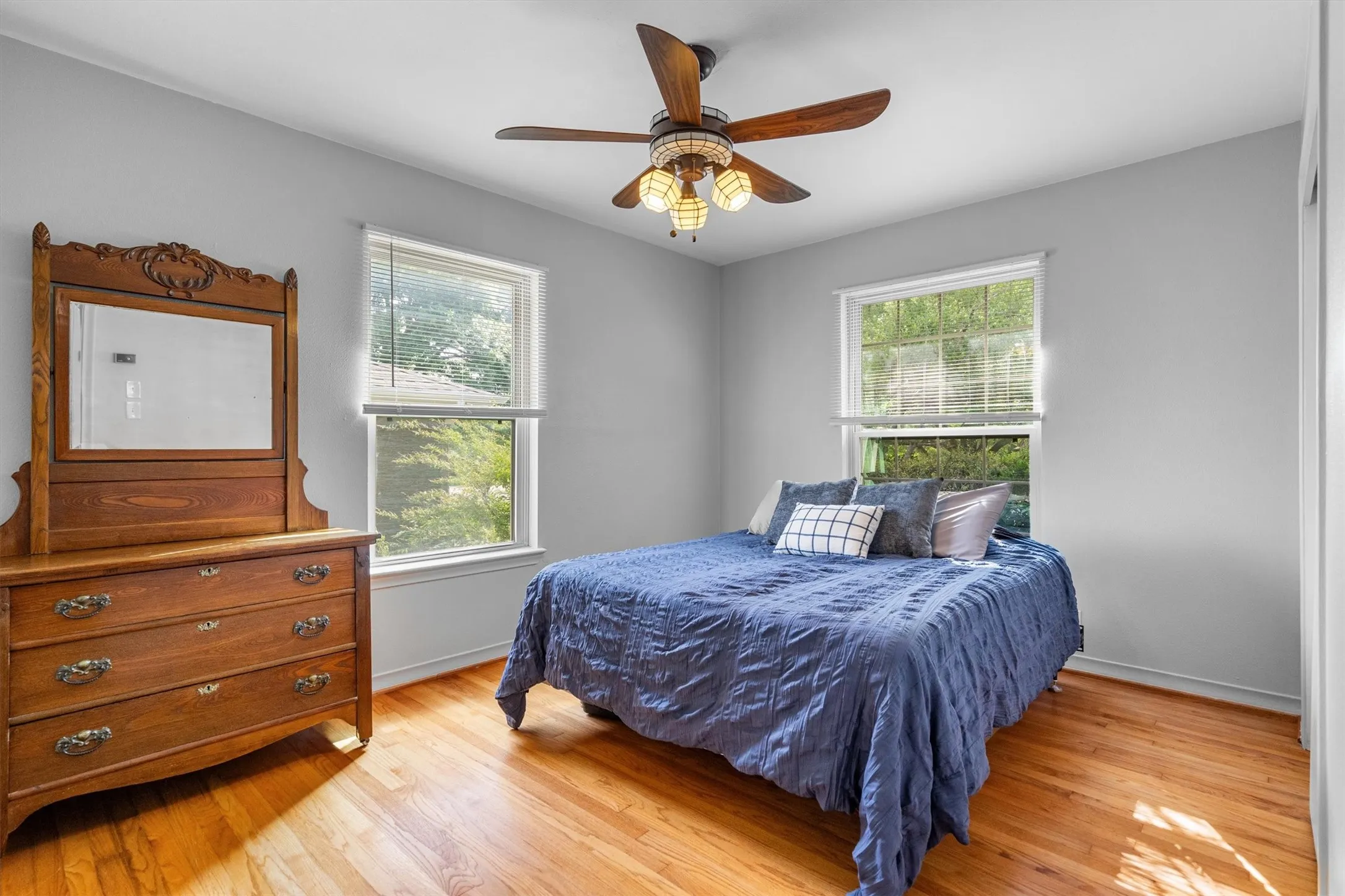 Light-filled room featuring wood-finish flooring, two large windows with blinds, a ceiling fan with integrated lighting, and neutral wall tones