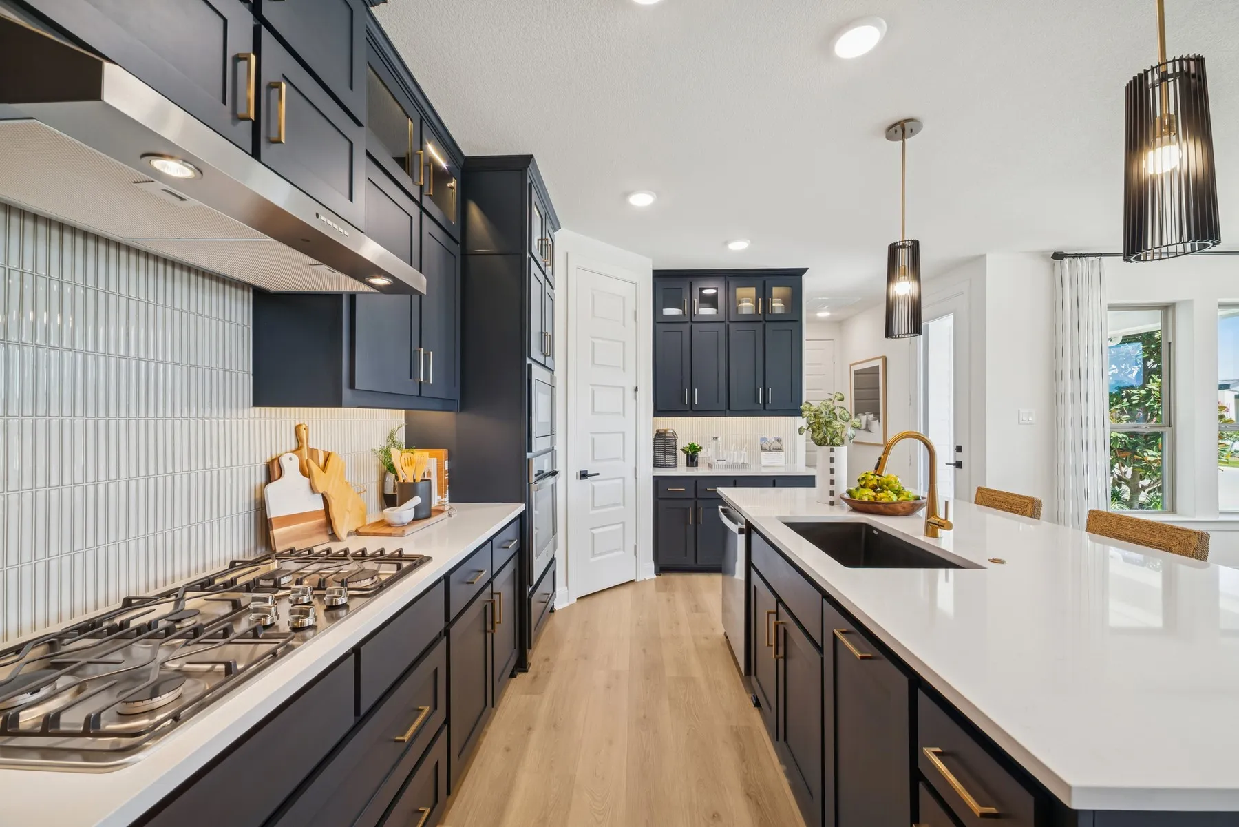 Modern kitchen featuring dark cabinetry, stainless steel appliances, a gas cooktop, and an expansive island with an undermount sink and gooseneck faucet