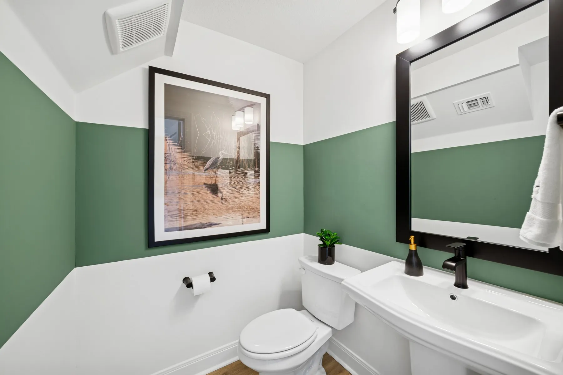 Pedestal sink with matte black faucet, wall-mounted mirror with black frame, and two-tone wall treatment
