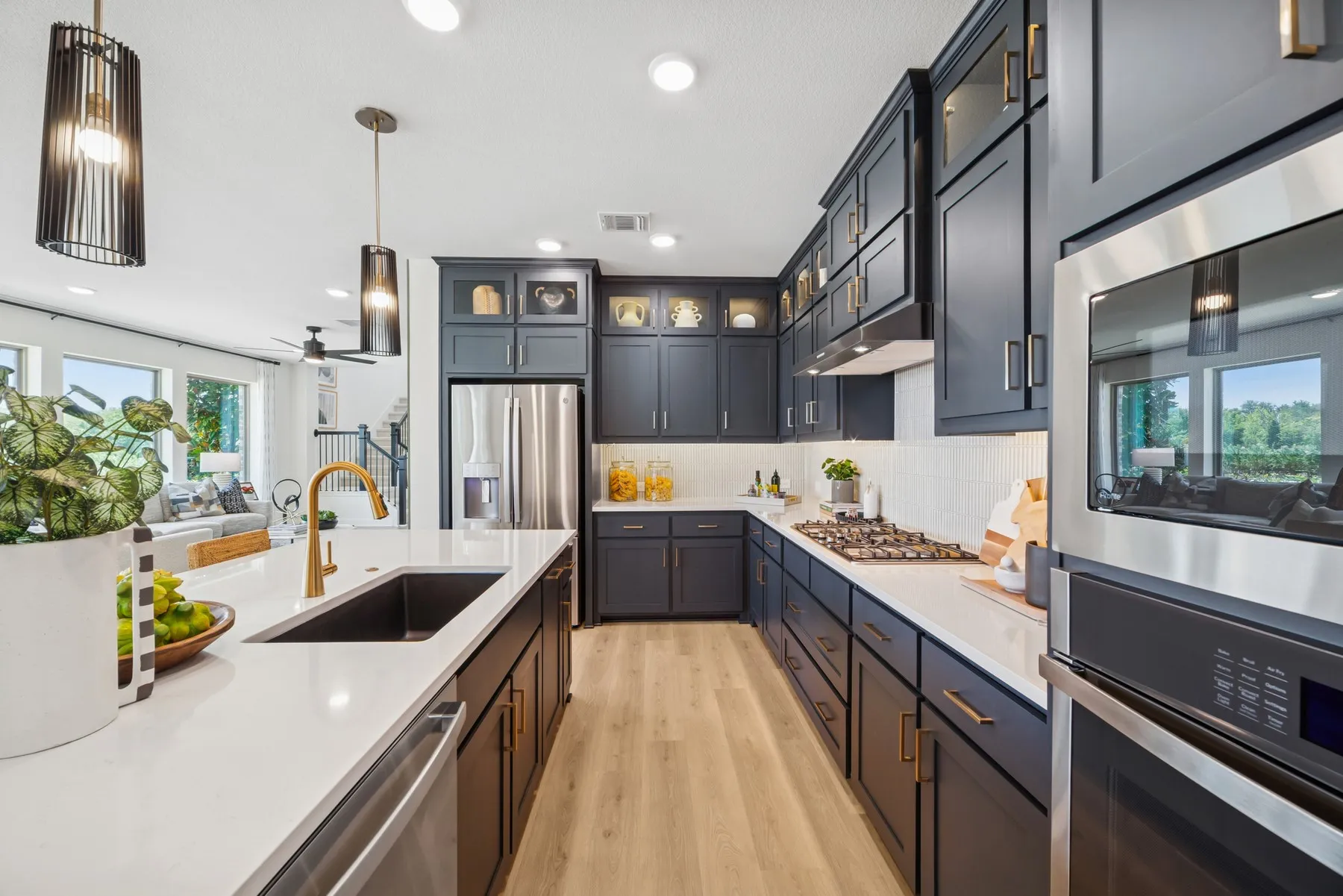 Gourmet kitchen featuring dark cabinetry, white countertops, stainless steel appliances, light wood-finish flooring, and pendant lighting
