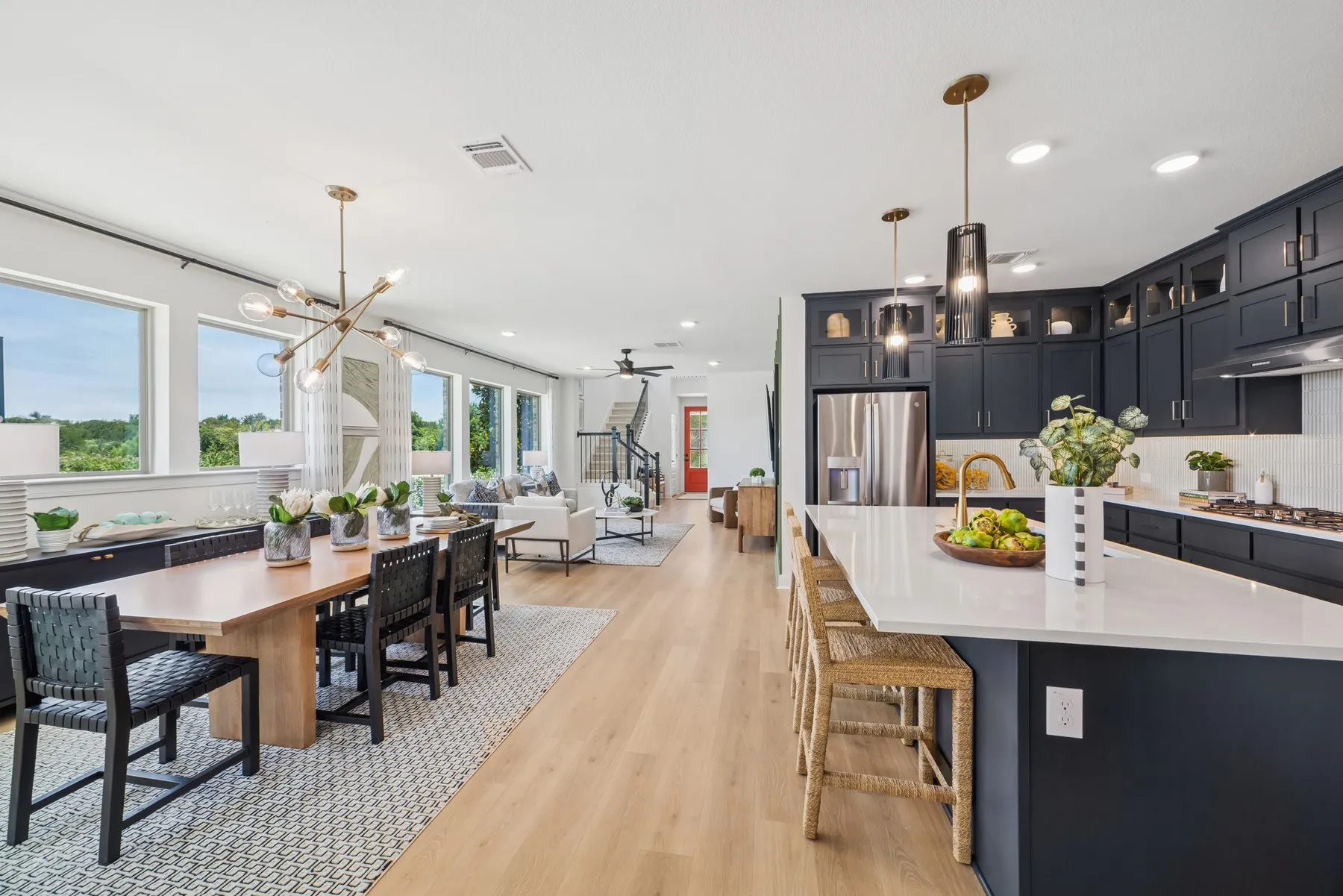Open-concept living space featuring wood-finish flooring throughout, a kitchen with dark cabinetry and a white countertop island, a dining area with a modern chandelier, and a living room with large windows