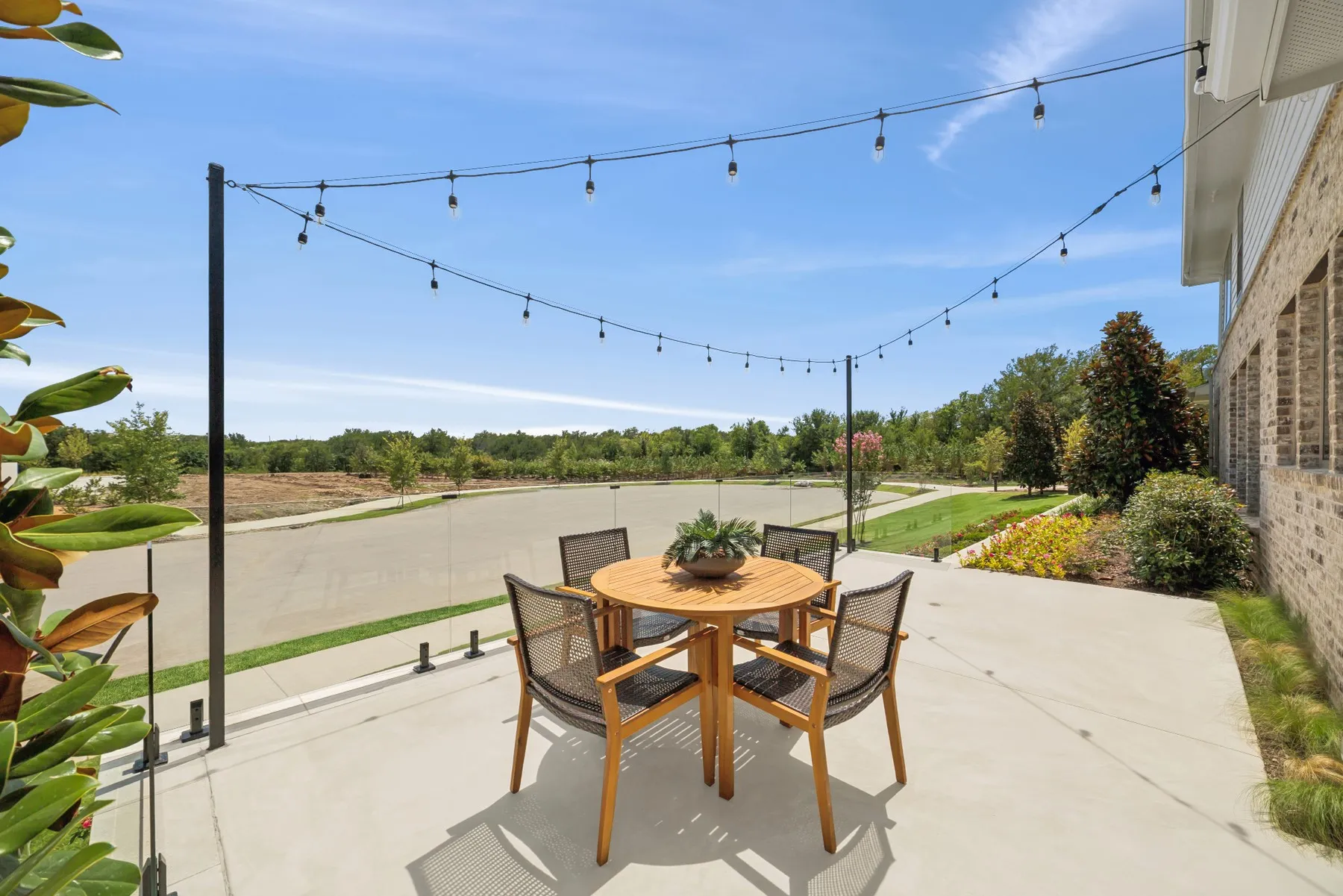 Outdoor patio featuring string lighting, a concrete surface, a glass railing, and a landscaped perimeter