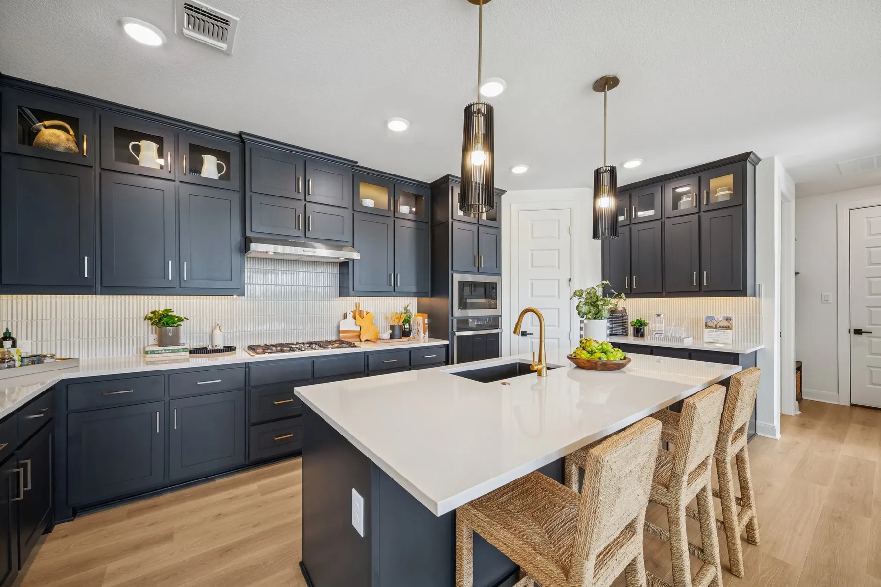 Kitchen featuring dark cabinetry, light countertops, wood-finish flooring, a central island with an integrated sink, and pendant lighting