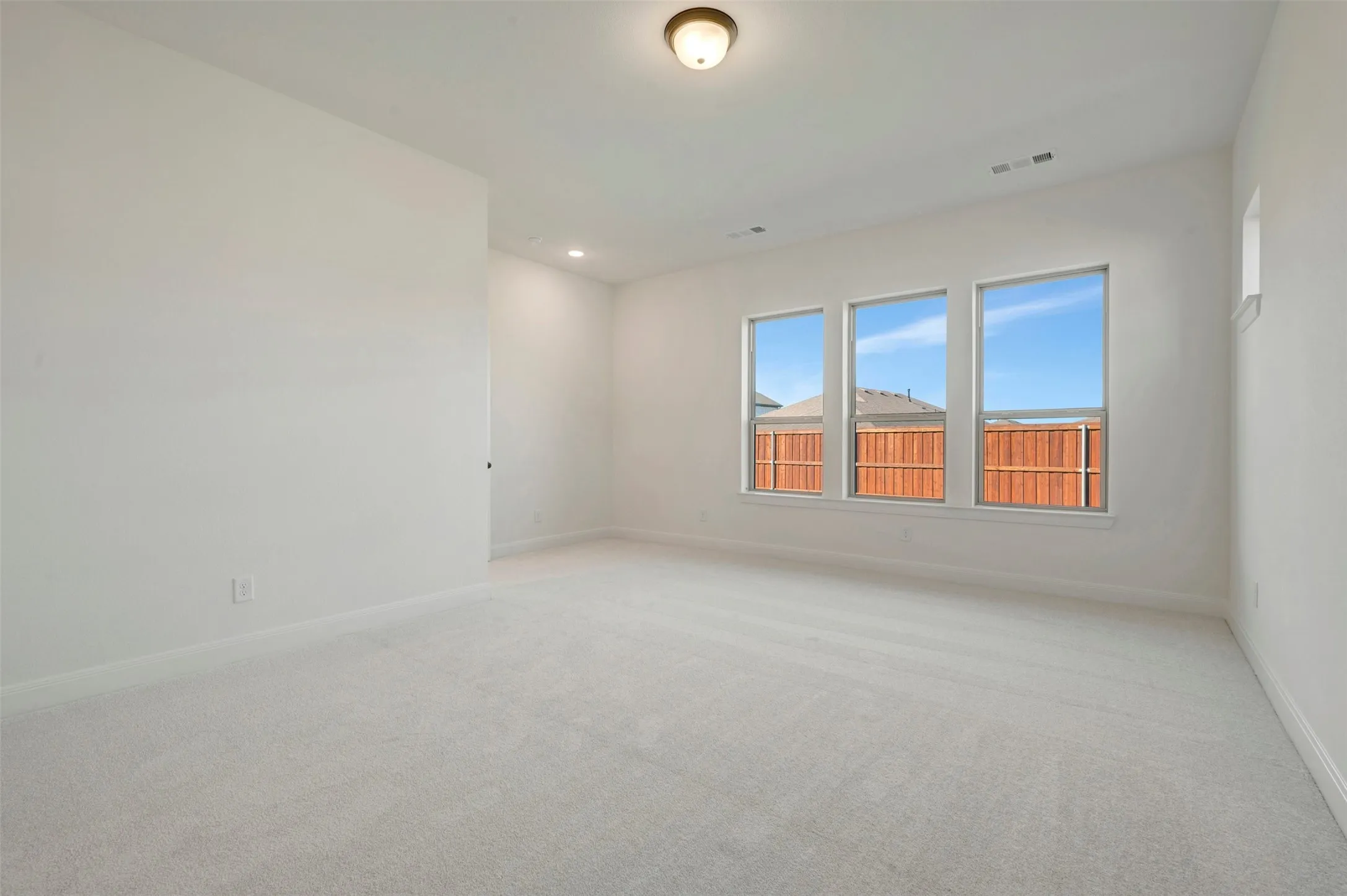 Spacious room featuring light-colored carpeting, multiple windows providing natural illumination, a flush-mount ceiling light fixture, and recessed lighting