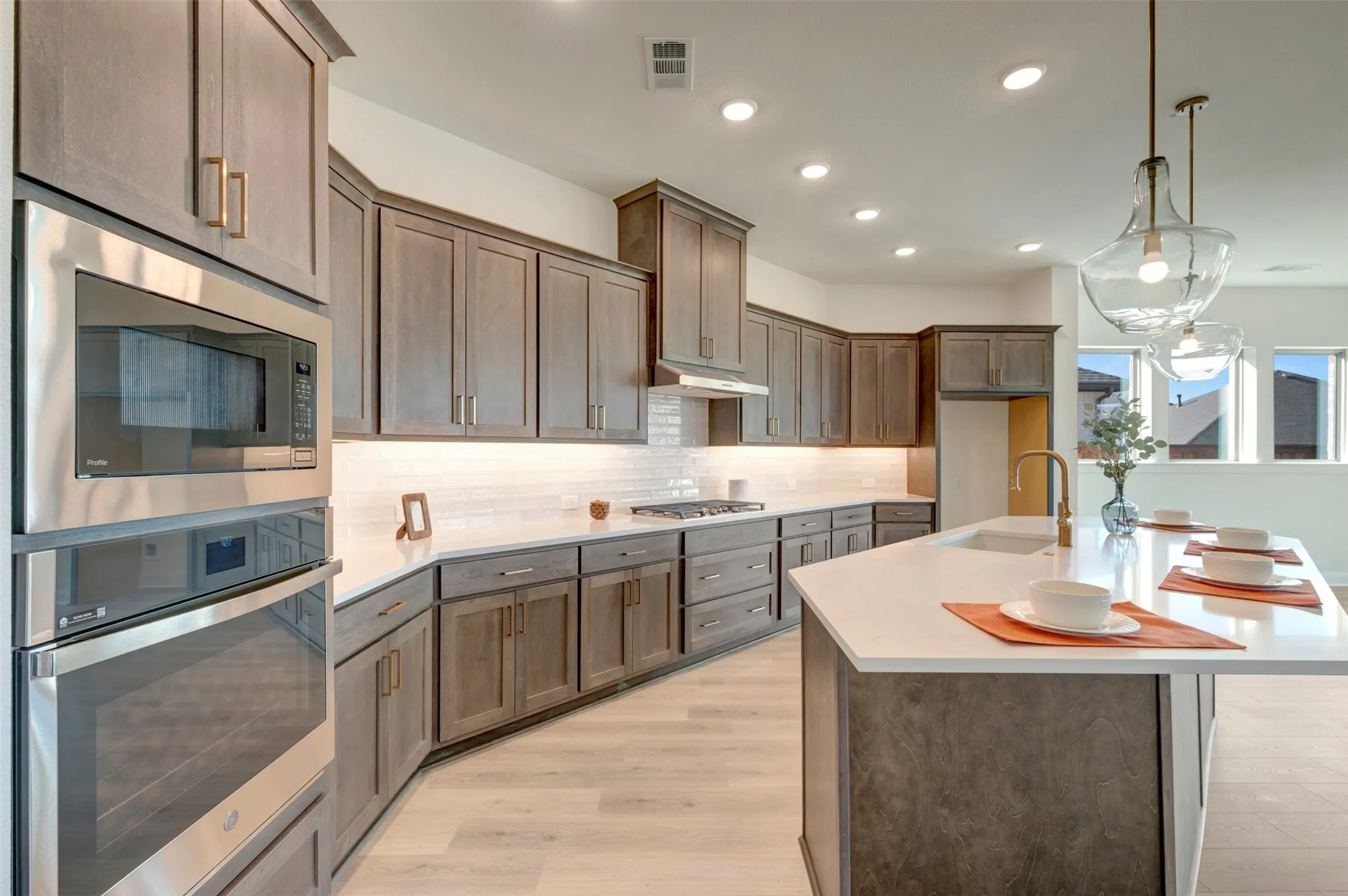 Spacious kitchen featuring extensive cabinetry, built-in stainless steel appliances, a large island with sink, pendant lighting, and wood-finish flooring
