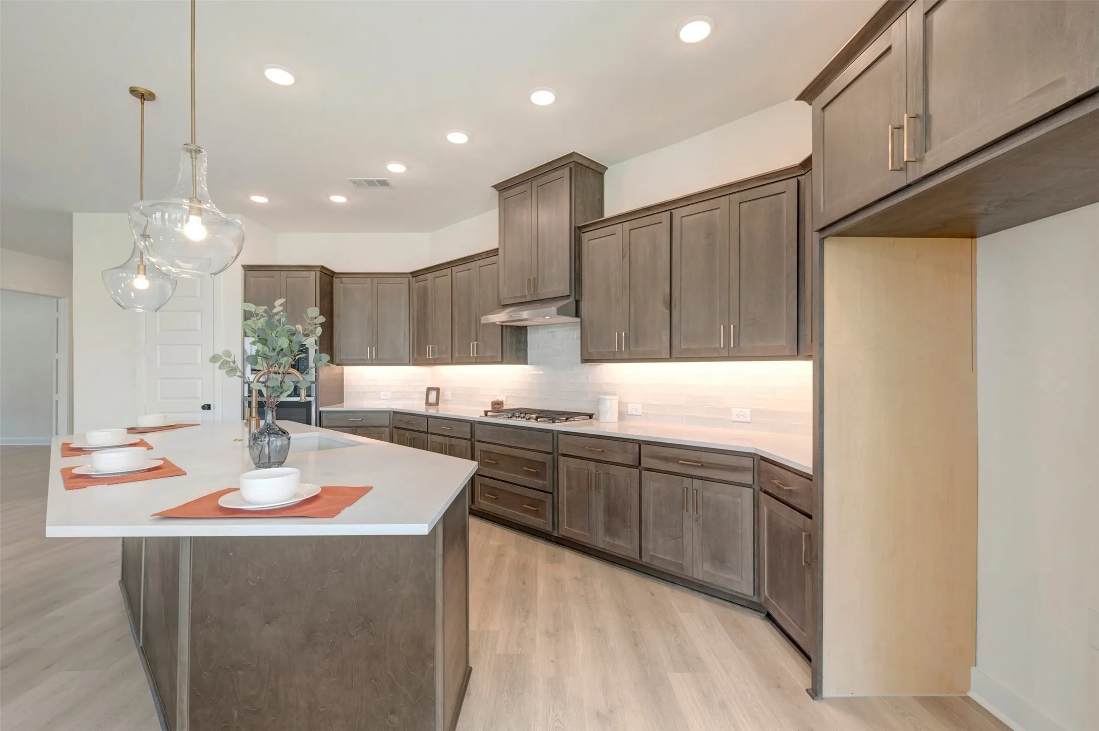 Kitchen featuring an expansive island with a white countertop, shaker-style cabinetry, wood-finish flooring, recessed lighting, and under-cabinet lighting