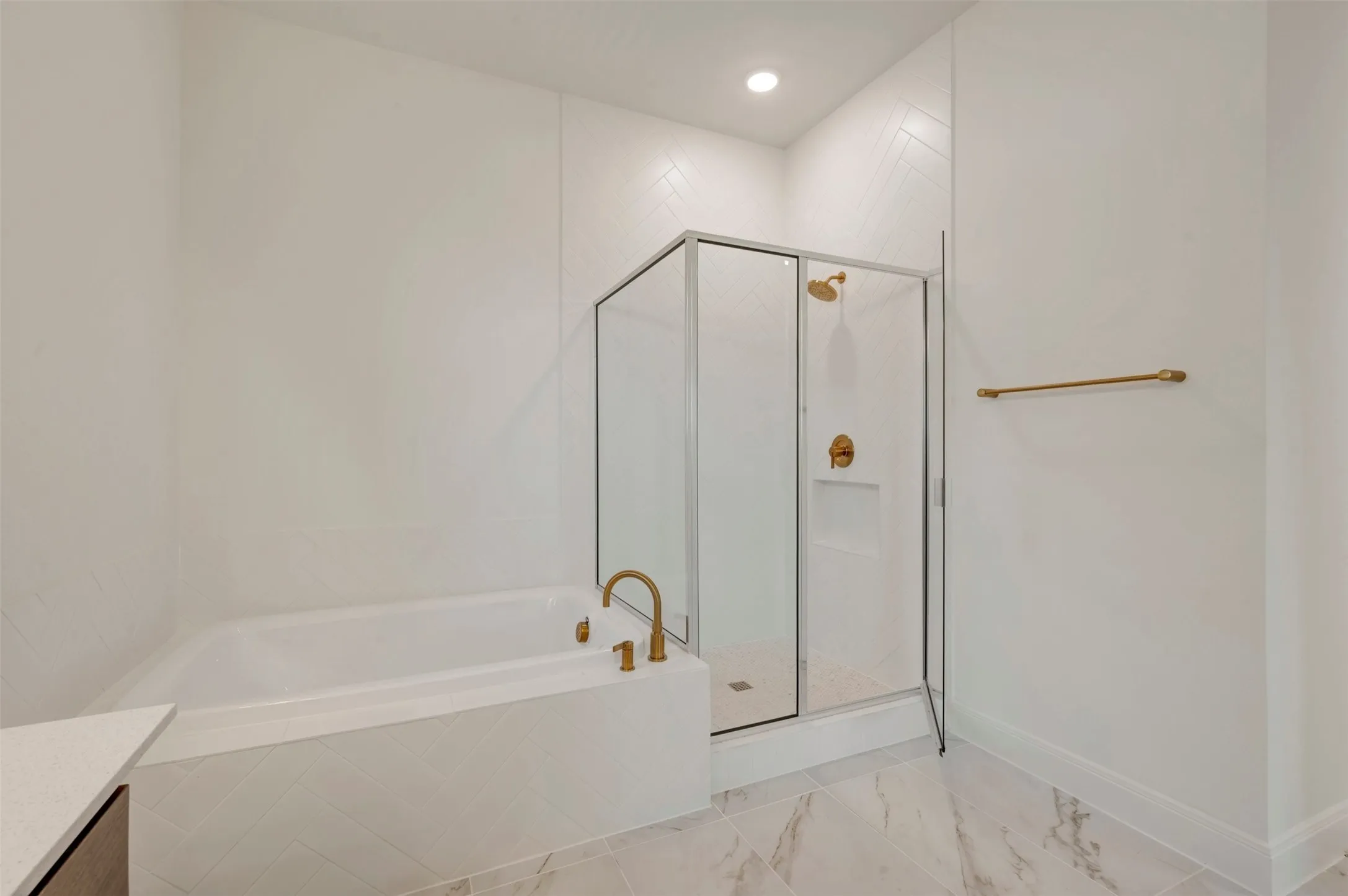 Bathtub with brass-finish fixtures, glass-enclosed shower, white tile walls, and large format floor tile