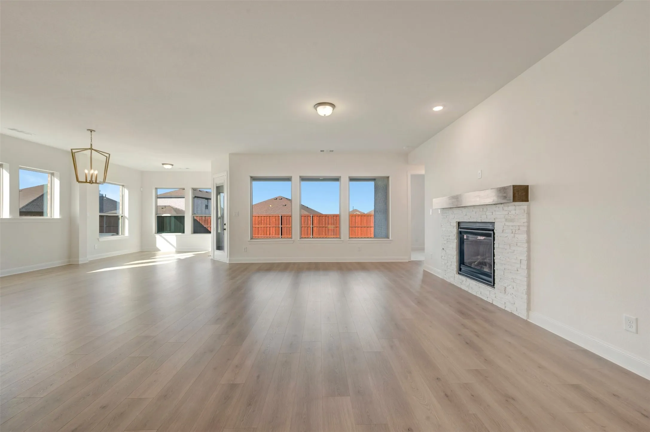 Spacious interior featuring wood-finish flooring, multiple windows, a decorative chandelier, recessed lighting, and a fireplace with a stacked stone surround