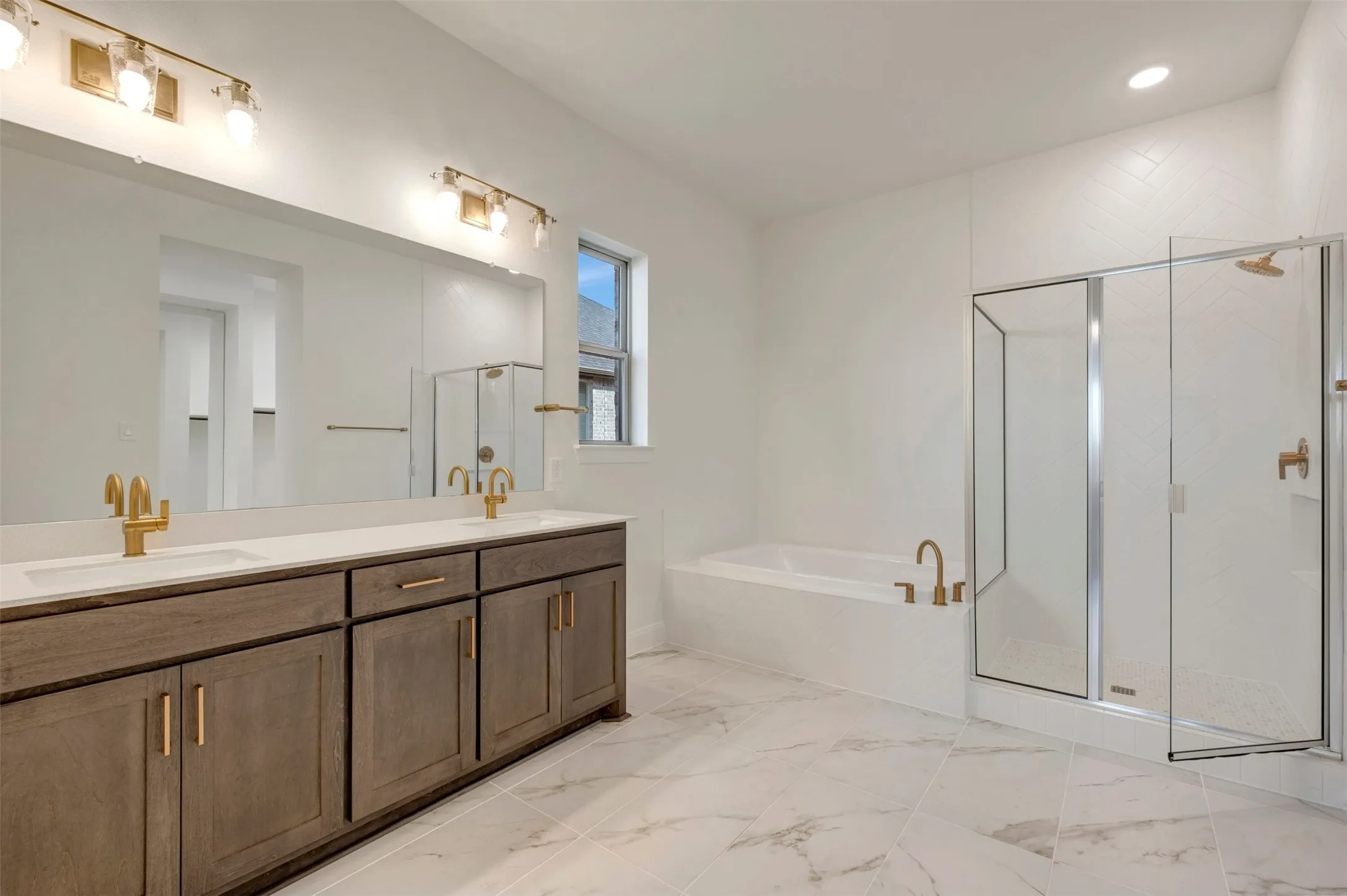 Dual vanity with gold-finish fixtures and hardware, large frameless mirror, separate walk-in shower with glass enclosure, and a soaking tub