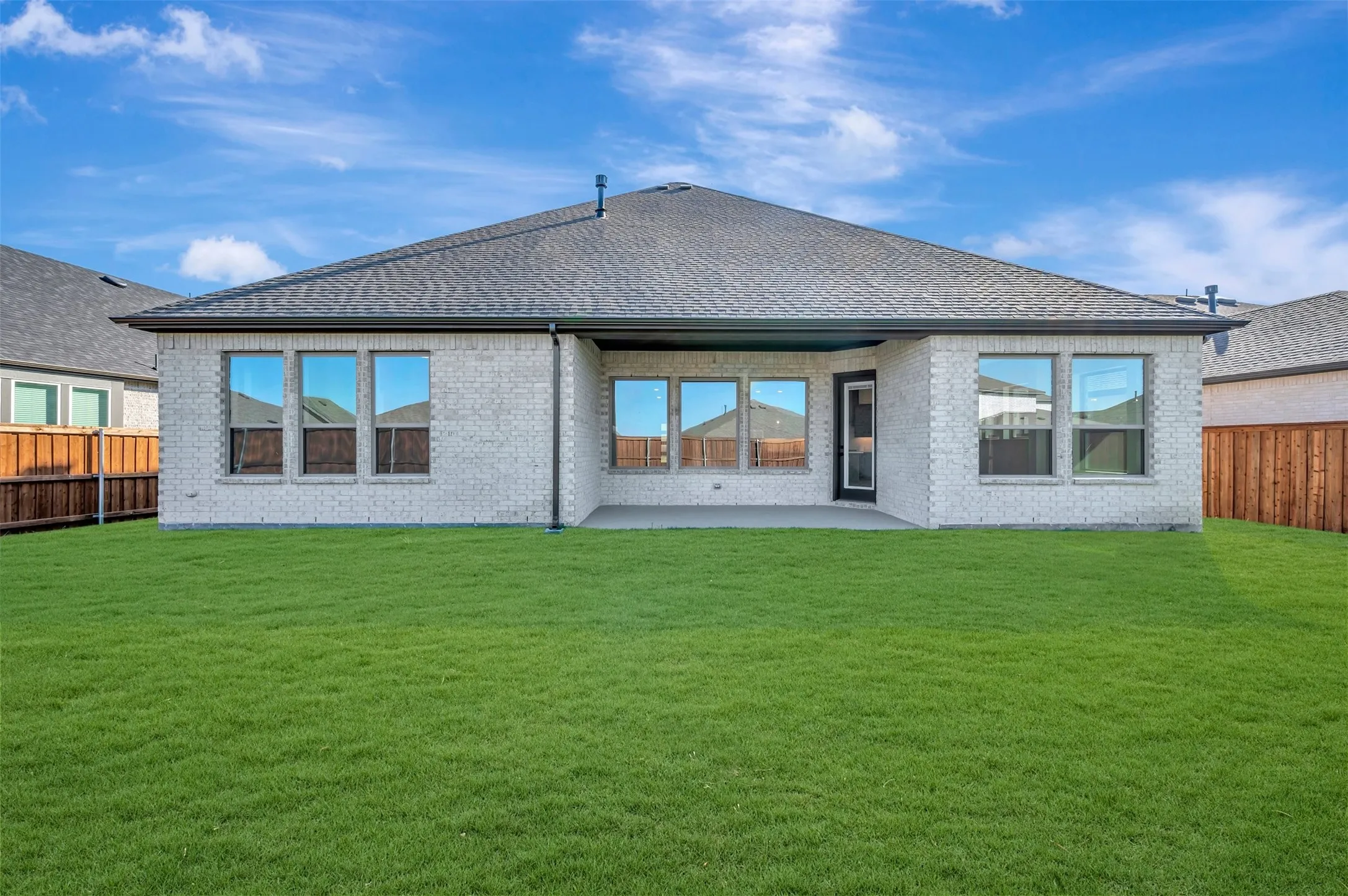 Expansive green lawn, brick exterior, multiple windows, covered patio, and a shingle roof