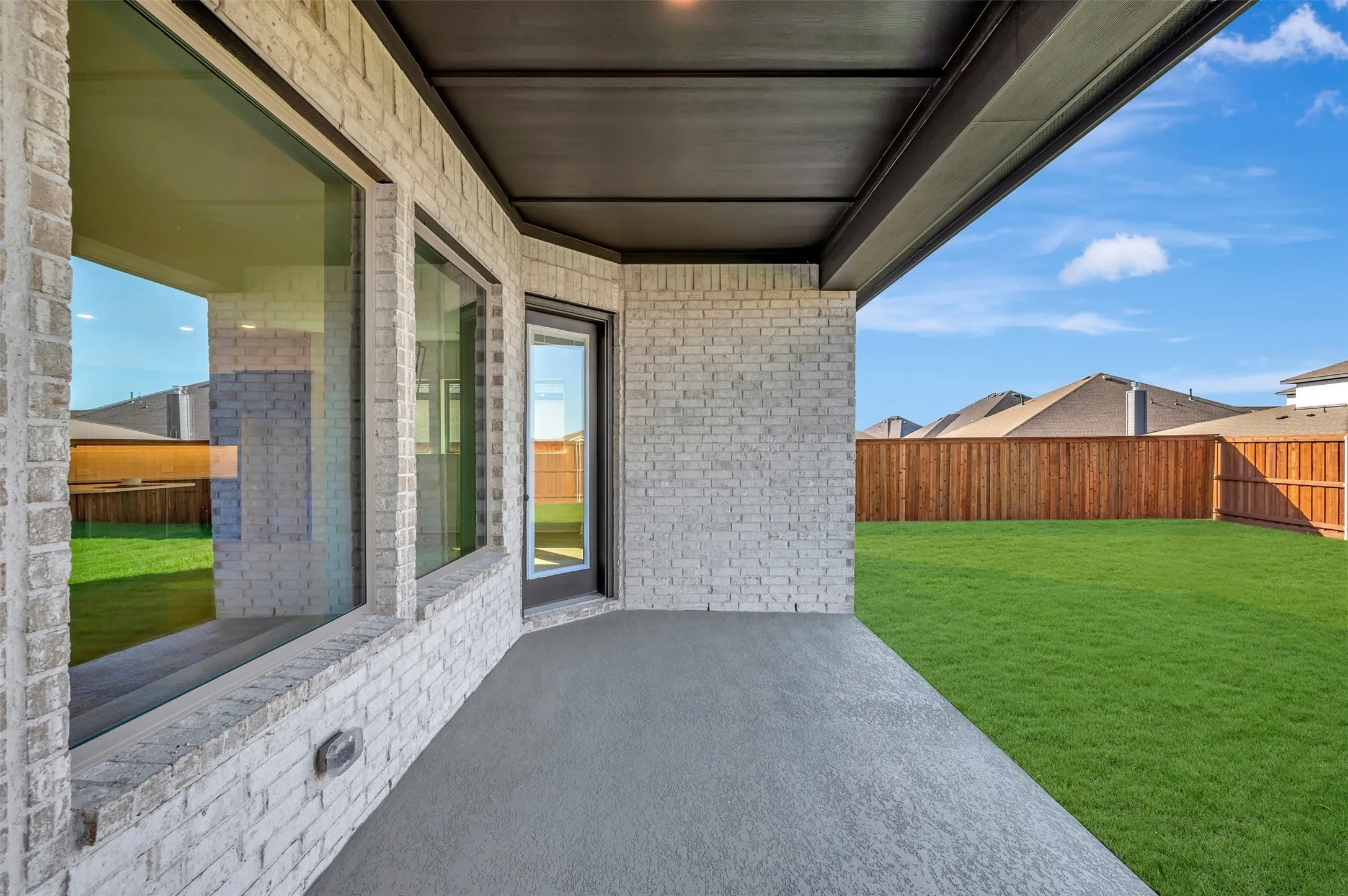 Paved patio with an overhead cover, brick exterior, large windows, and a fenced yard with a manicured lawn