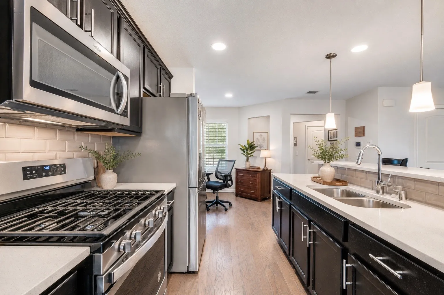 Modern kitchen featuring stainless steel appliances, dark wood cabinetry, light-toned countertops, subway tile backsplash, and wood-finish flooring