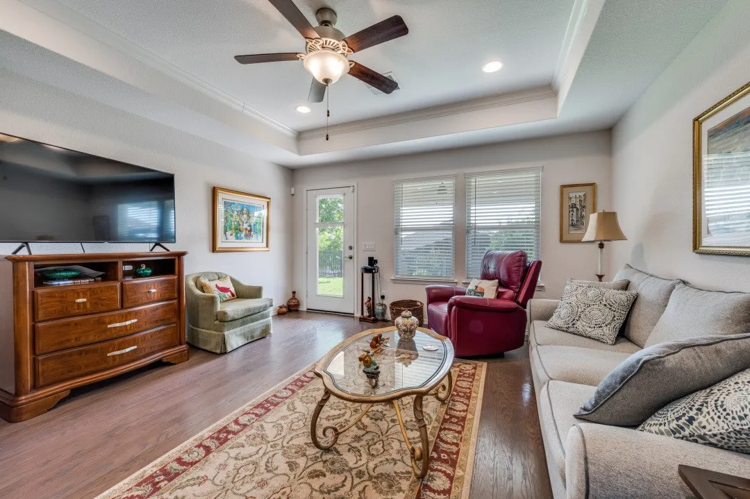 Living area featuring wood-finish flooring, a tray ceiling with recessed lighting and a ceiling fan, and multiple windows with blinds