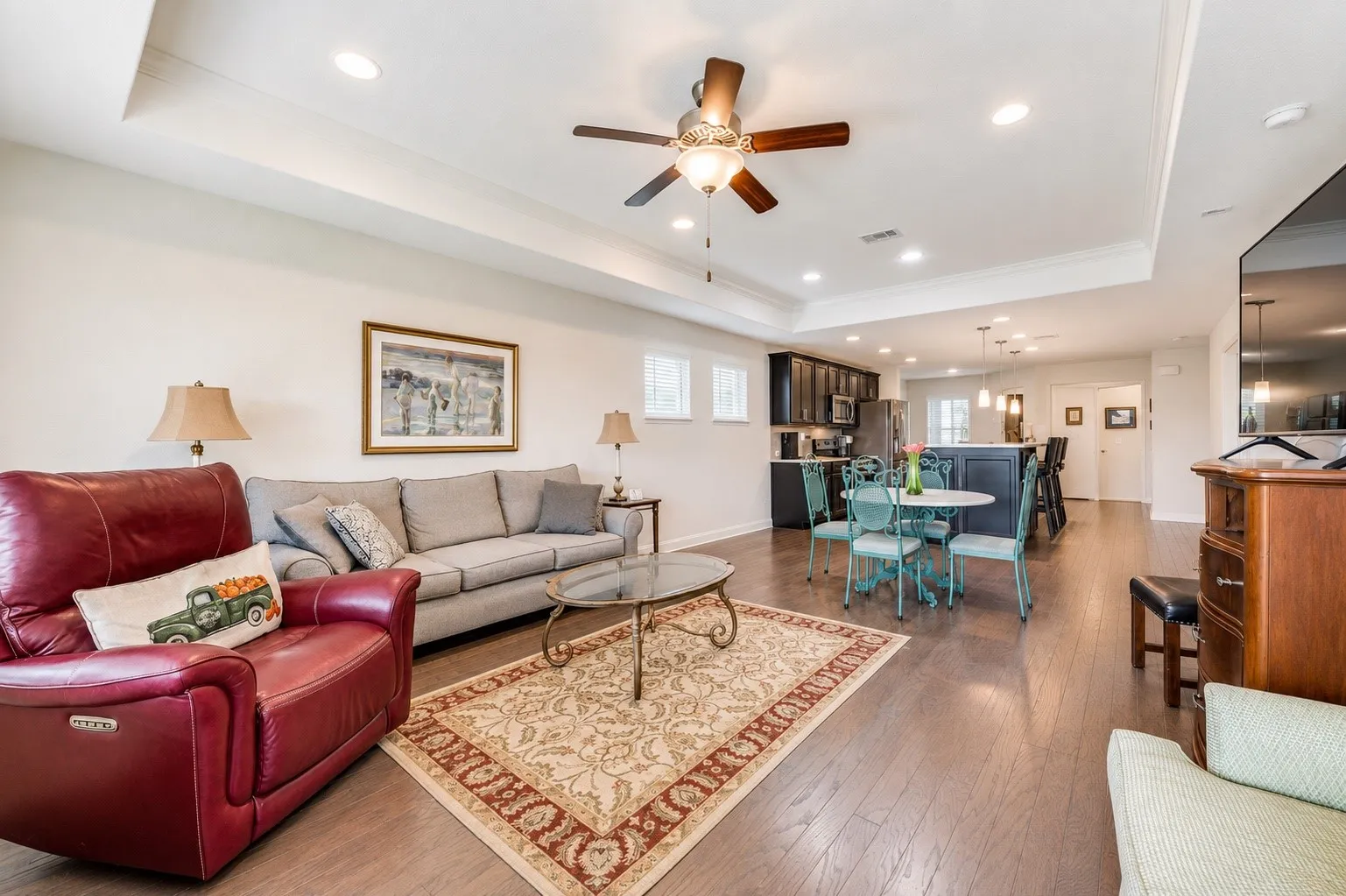 Open-concept living space featuring wood-finish flooring, recessed lighting, and a tray ceiling with a ceiling fan