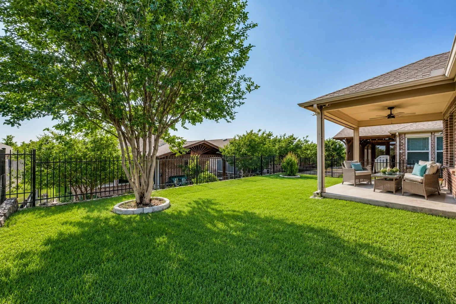 Expansive green lawn with a mature tree, bordered by a black metal fence
