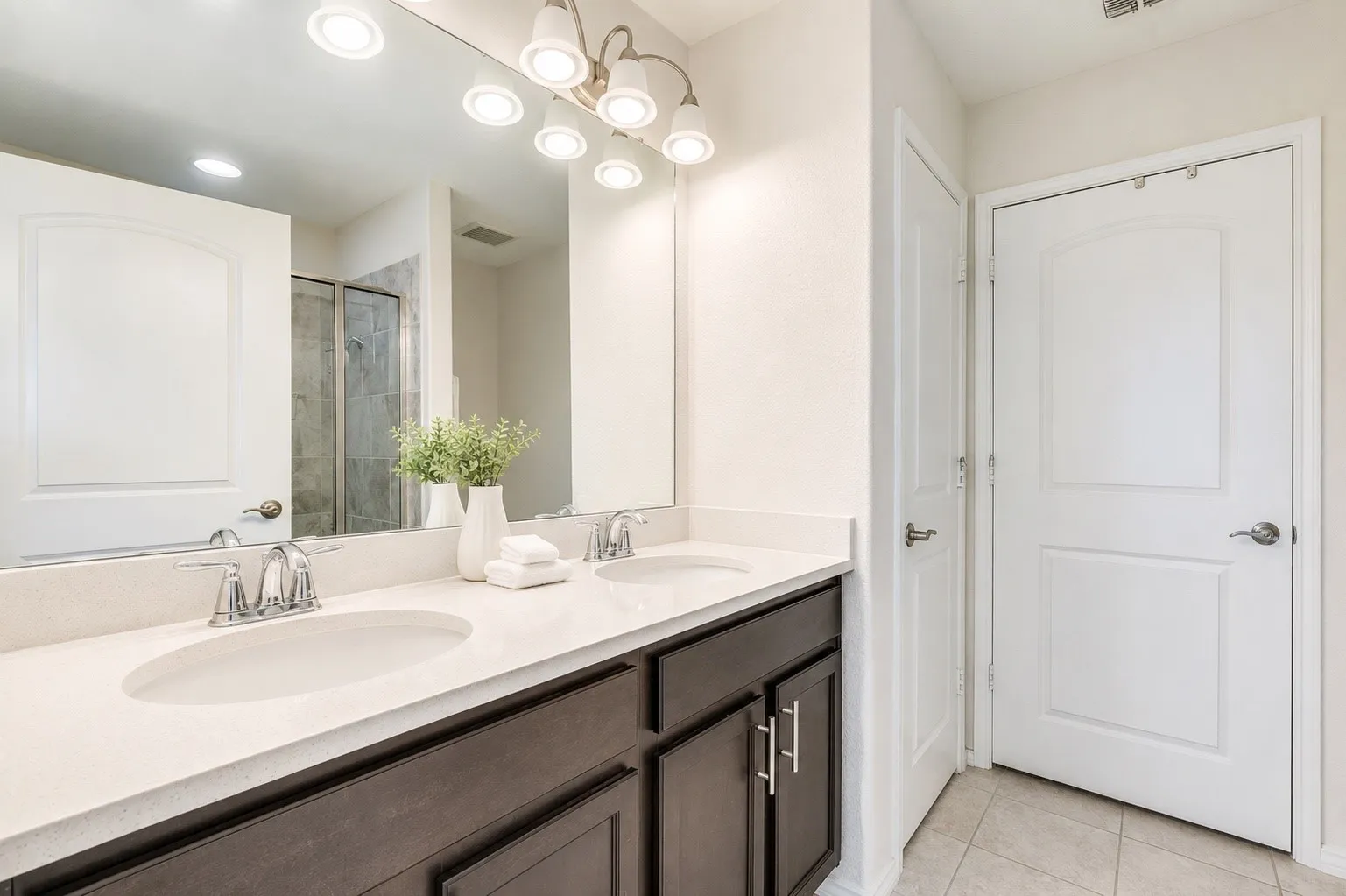 Dual undermount sinks set within a light-toned countertop, featuring a dark wood-finish vanity with chrome hardware