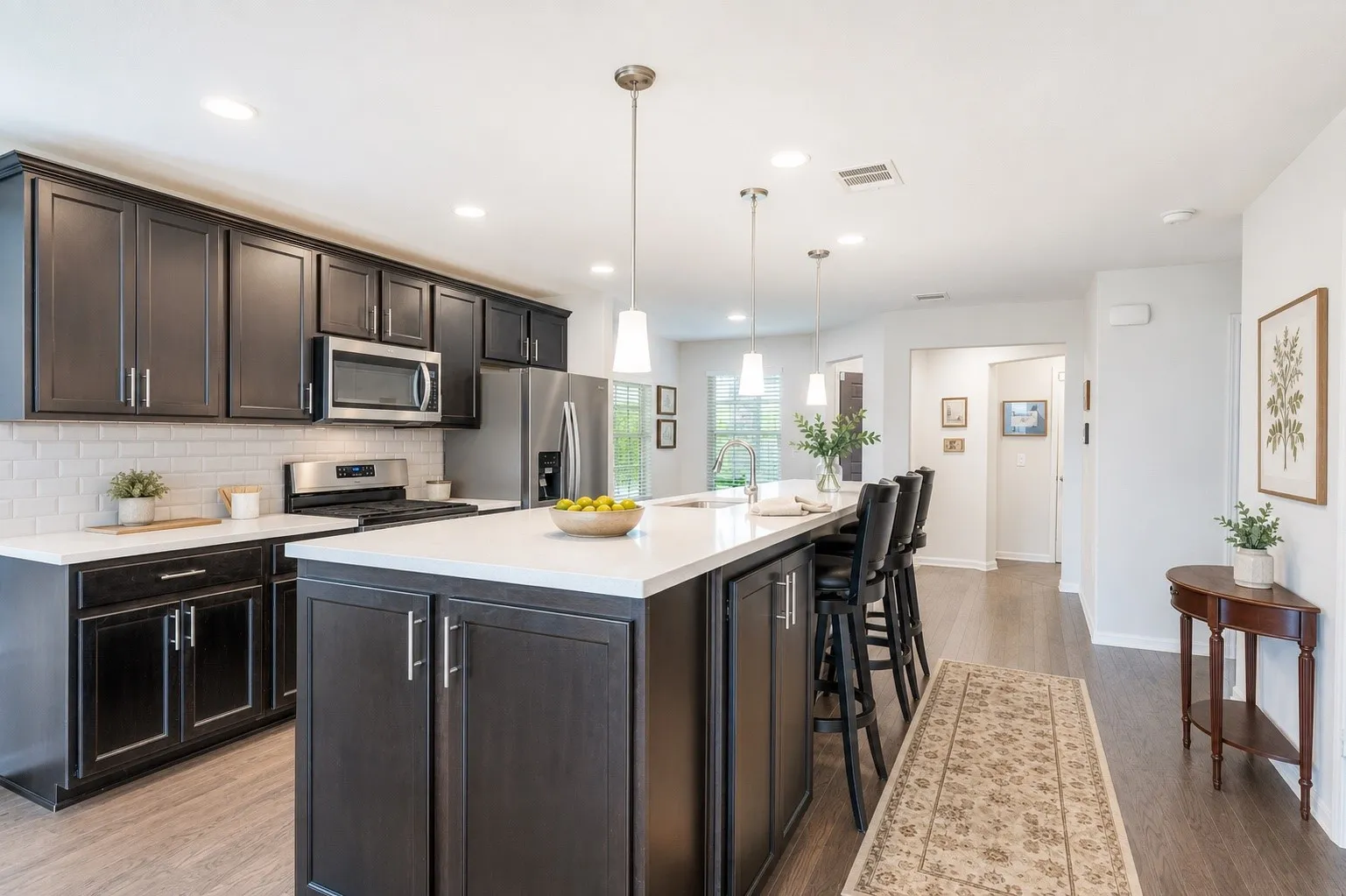 Modern kitchen featuring dark wood-finish cabinetry, stainless steel appliances, a white subway tile backsplash, and a large central island with seating and pendant lighting