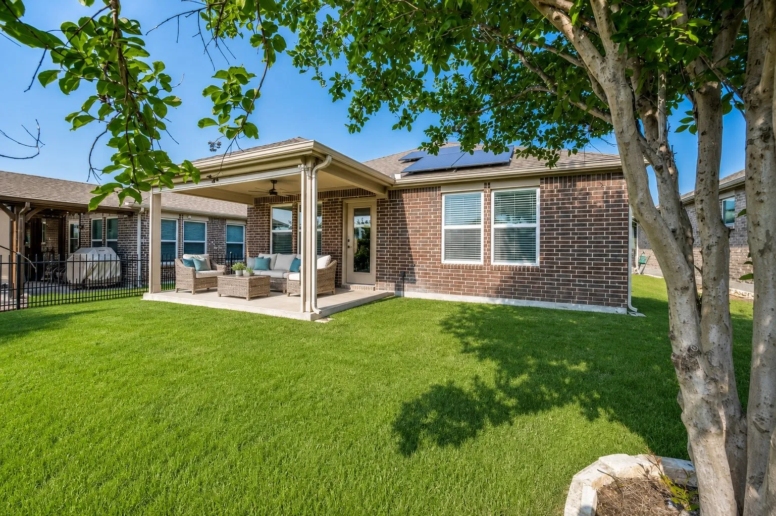 Expansive backyard featuring a covered patio, brick exterior, multiple windows, and solar panels