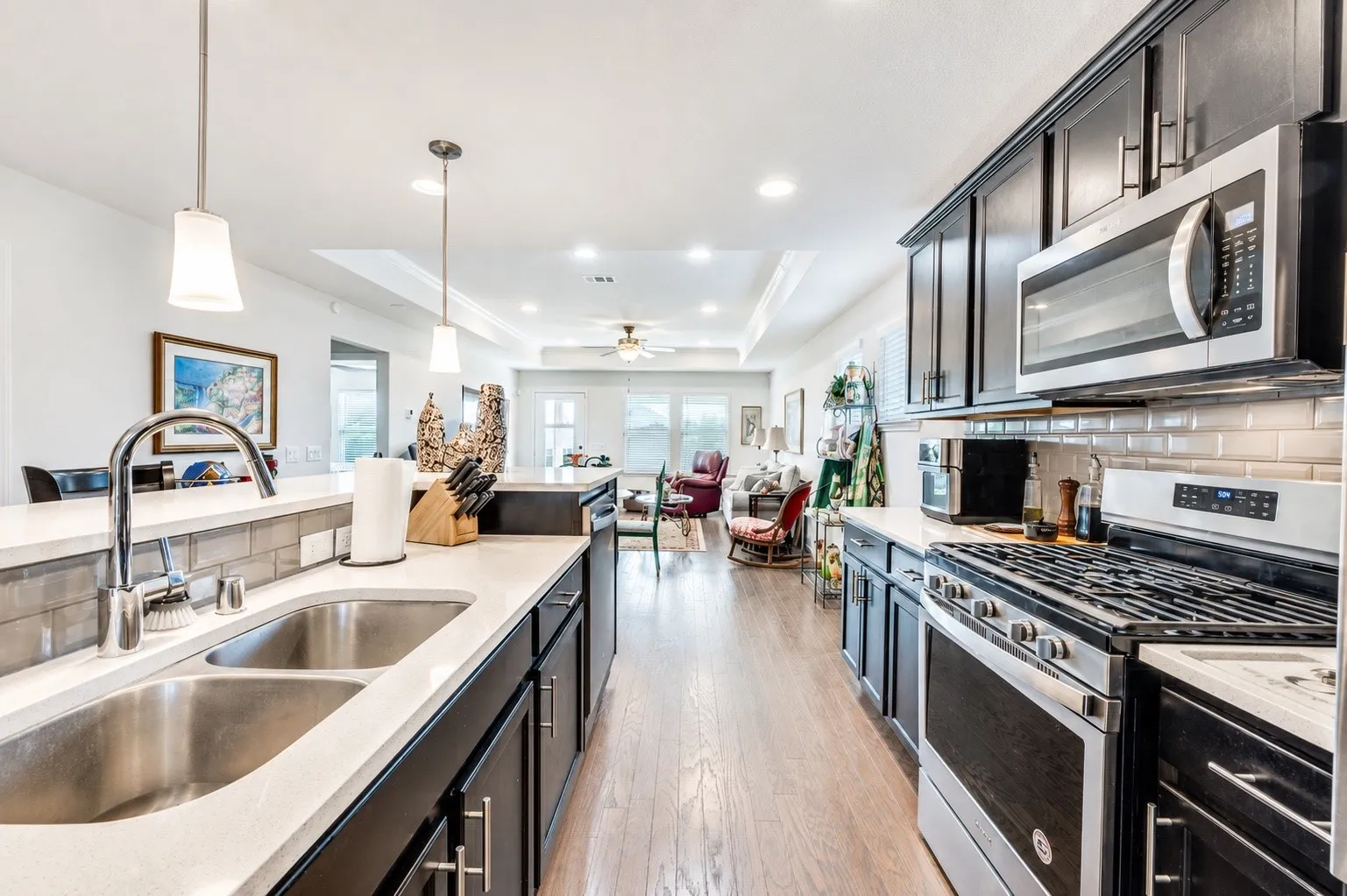 Kitchen featuring a dual basin sink with gooseneck faucet, light-toned countertops, dark cabinetry, and stainless steel appliances, including a gas range and built-in microwave