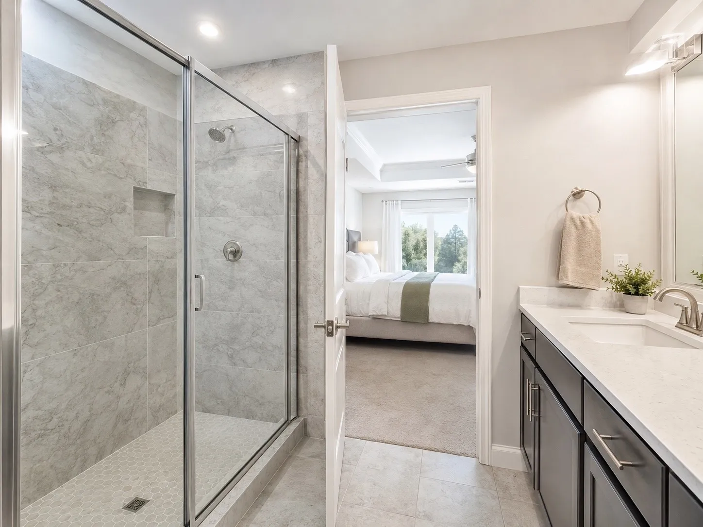 Spacious bathroom featuring a glass-enclosed shower with gray tiled walls and a hex-tiled floor, a single vanity with a white countertop and dark cabinetry, and brushed nickel fixtures