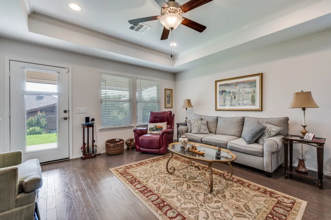Spacious living area featuring wood-finish flooring, a tray ceiling with recessed lighting, and a ceiling fan