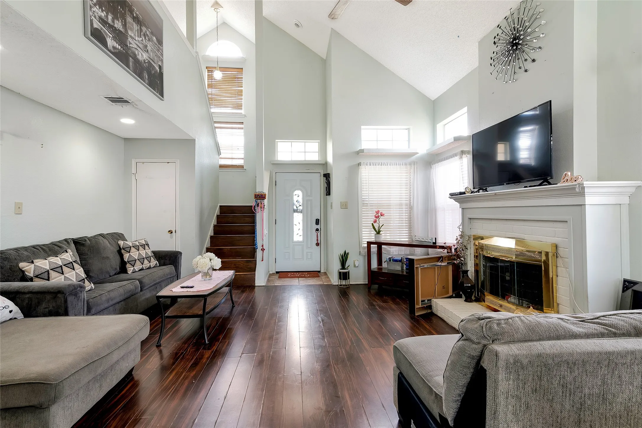 Living room with dark wood-type flooring, a brick fireplace, and high vaulted ceiling