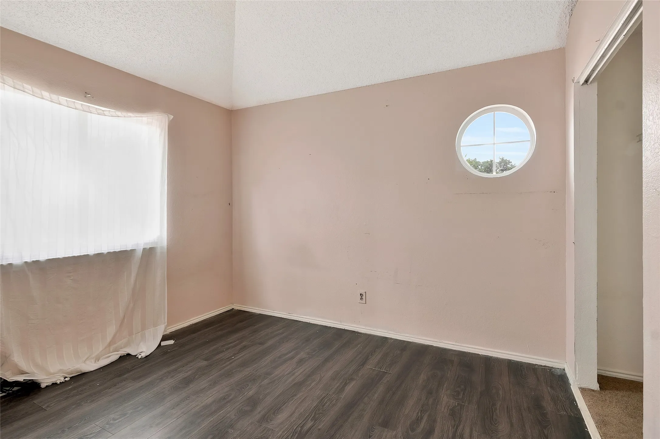 Empty room with lofted ceiling, hardwood / wood-style floors, and a textured ceiling