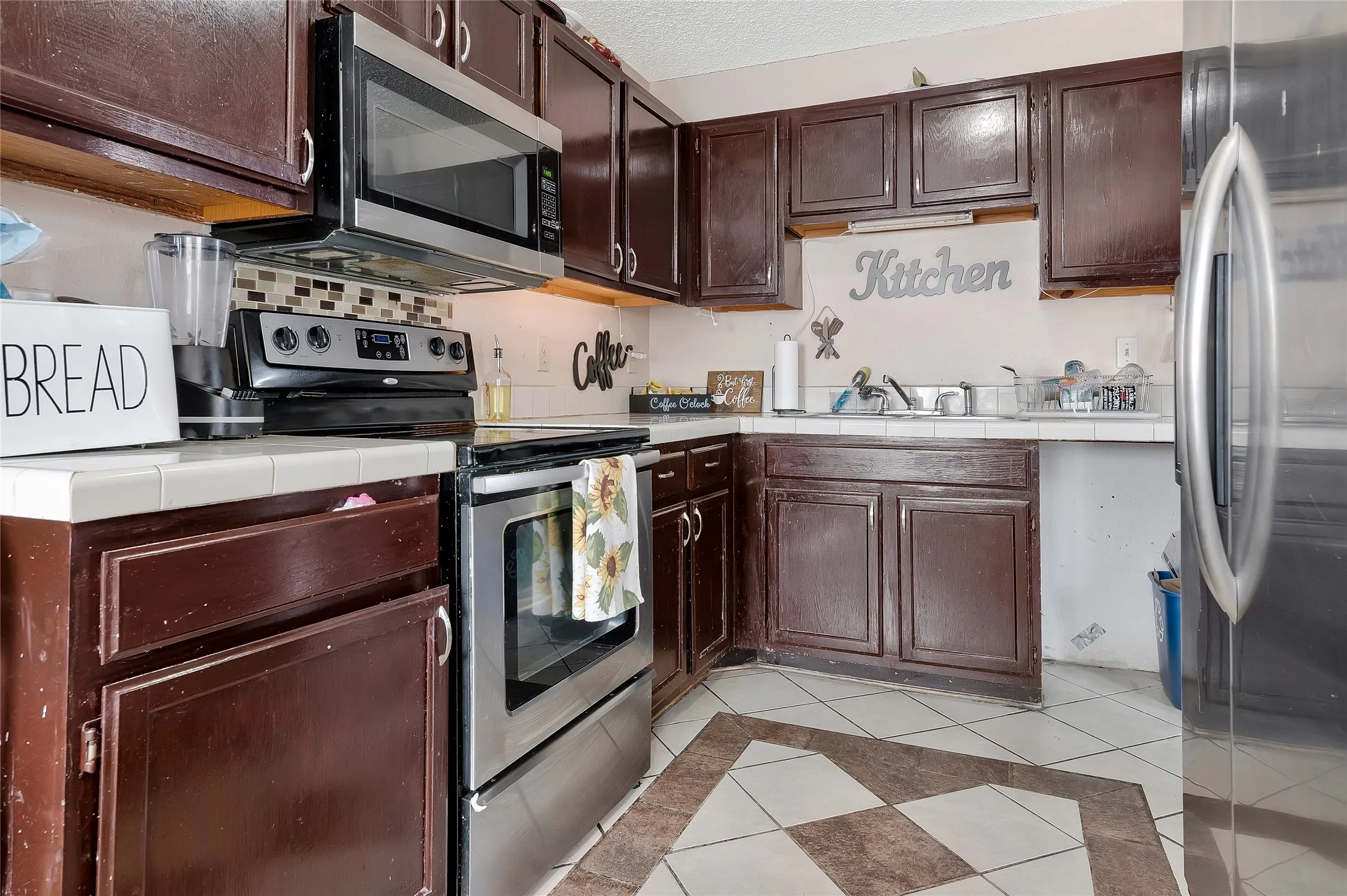Kitchen with tile countertops, light tile patterned floors, and stainless steel appliances