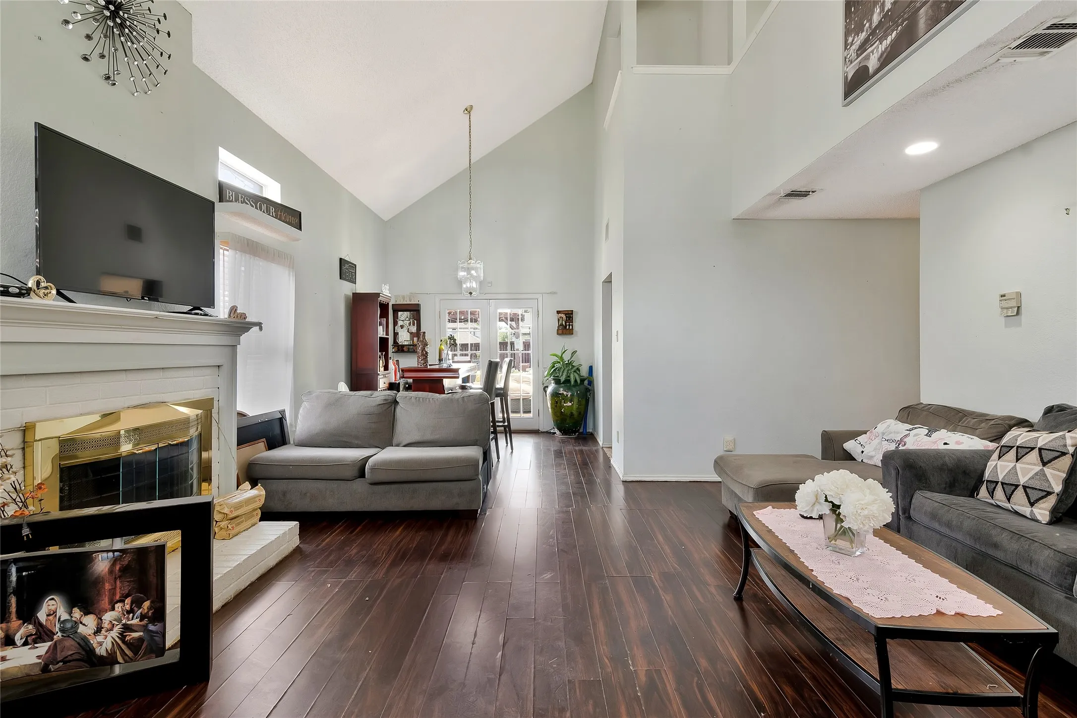 Living room with an inviting chandelier, dark wood-type flooring, french doors, and high vaulted ceiling