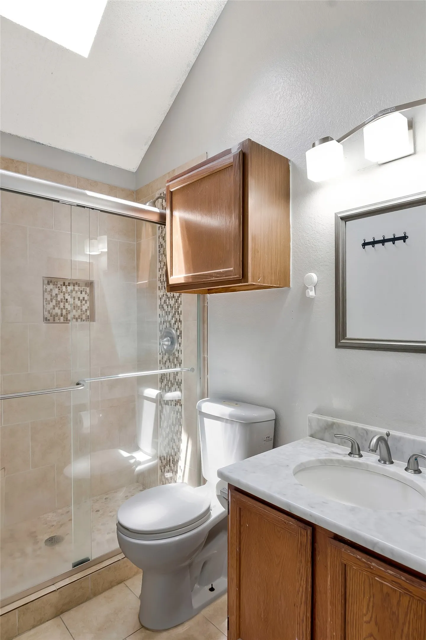 Bathroom featuring vanity, an enclosed shower, vaulted ceiling, toilet, and tile patterned flooring