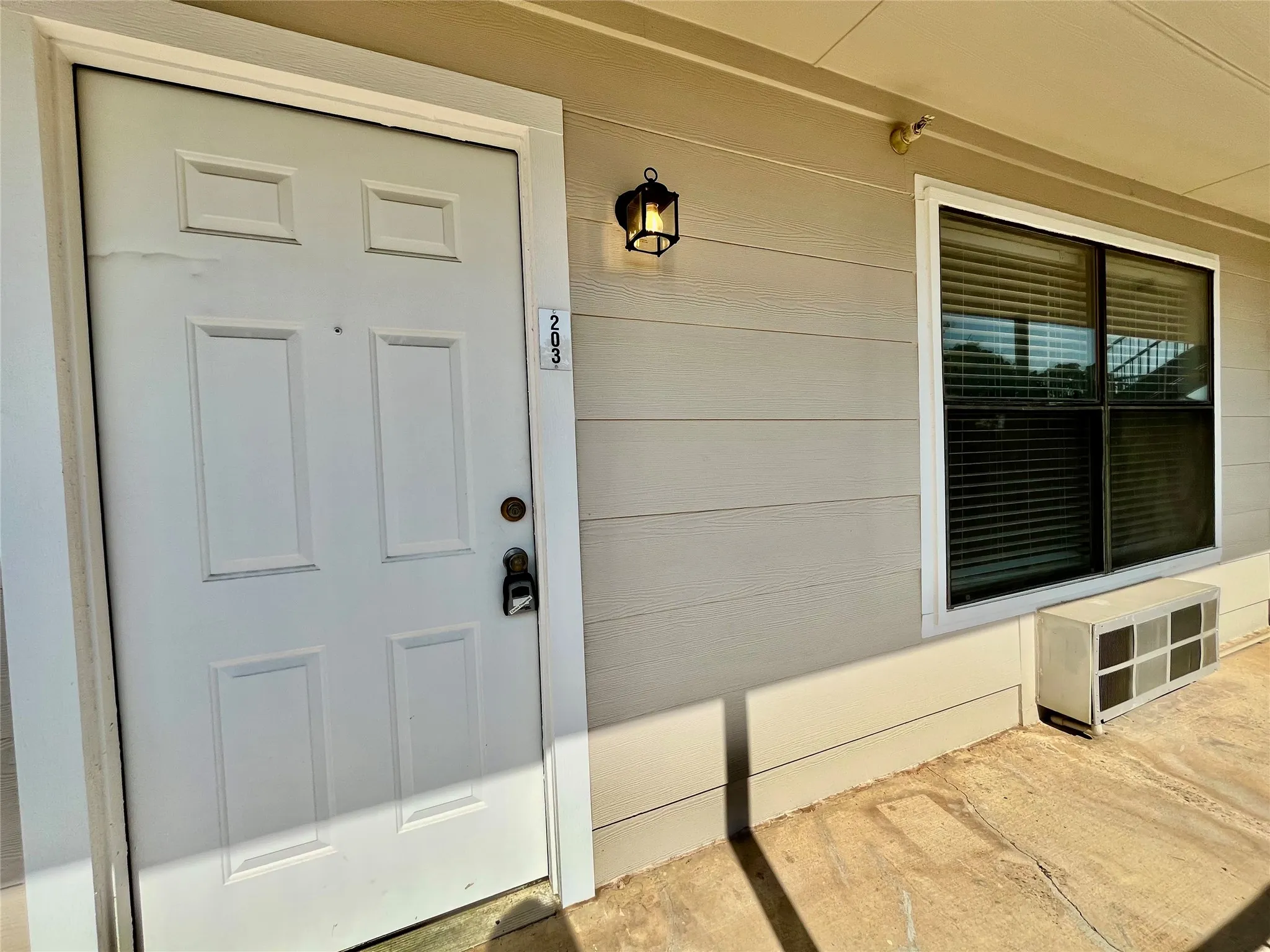 Clean and inviting unit entrance featuring neutral siding, a secure door, and updated exterior lighting.
