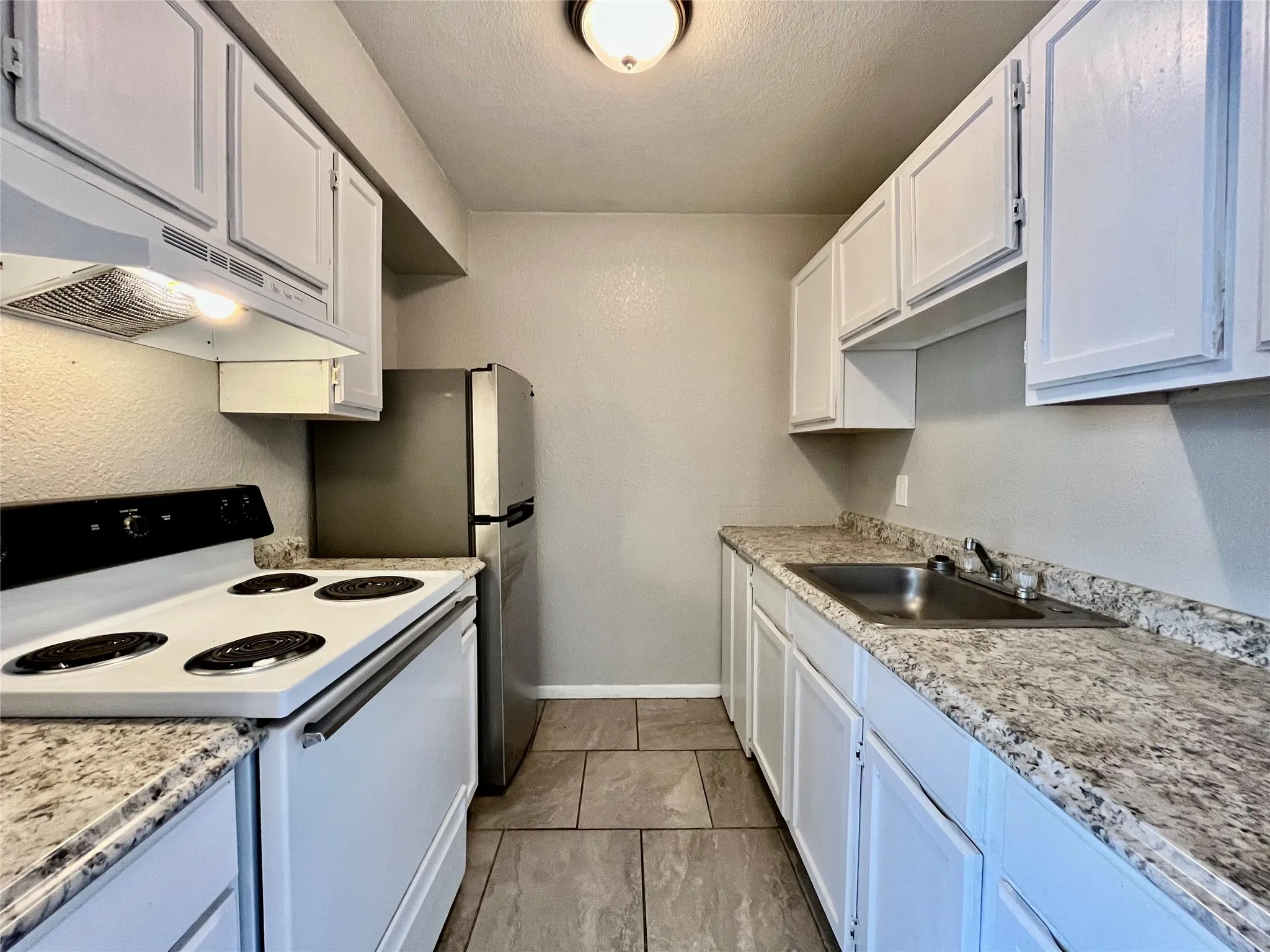 Updated galley kitchen featuring stylish granite-look countertops and a sleek stainless steel refrigerator.