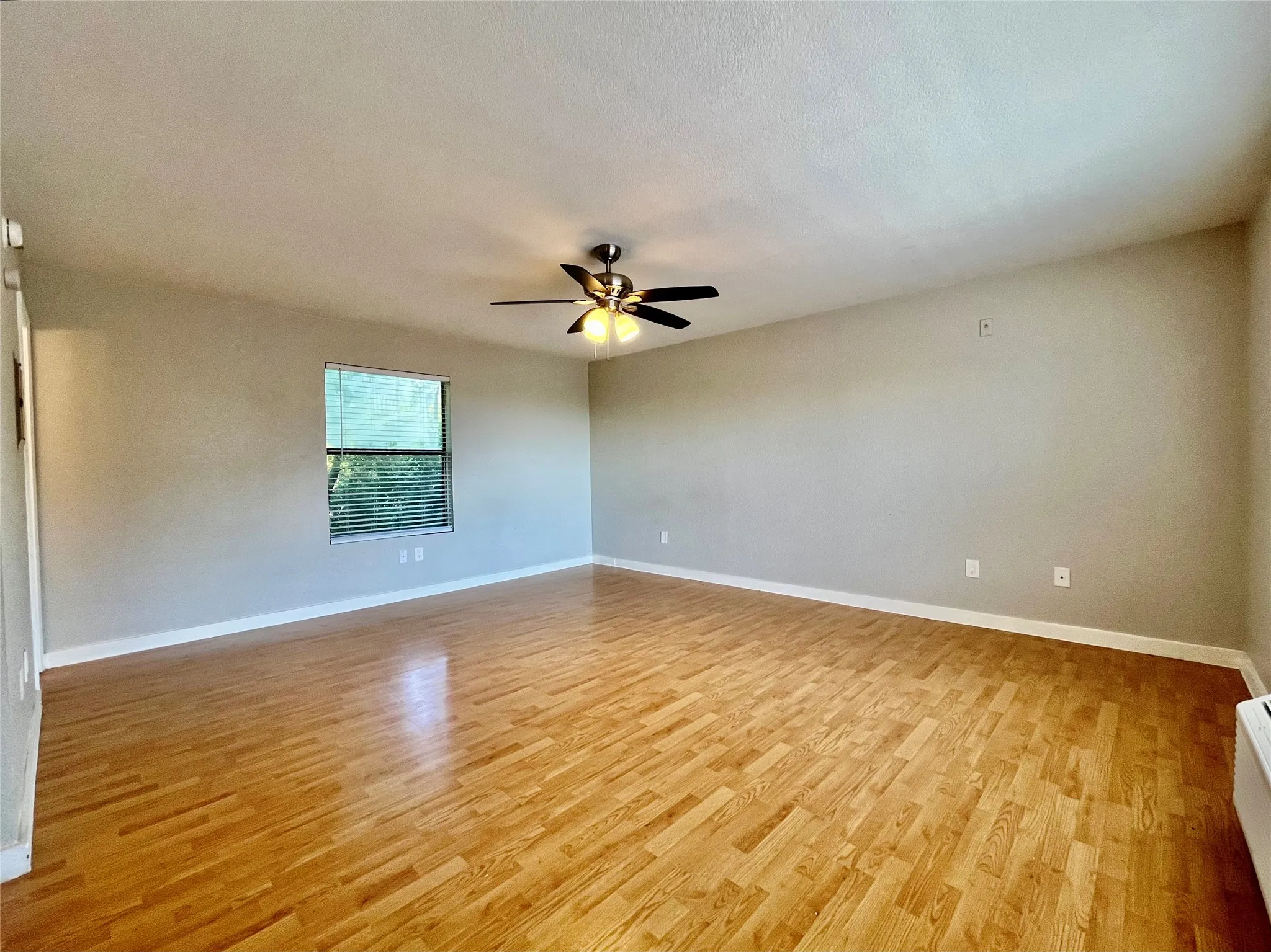 Bright, open-concept living area with warm honey-toned flooring and a large window for natural light.