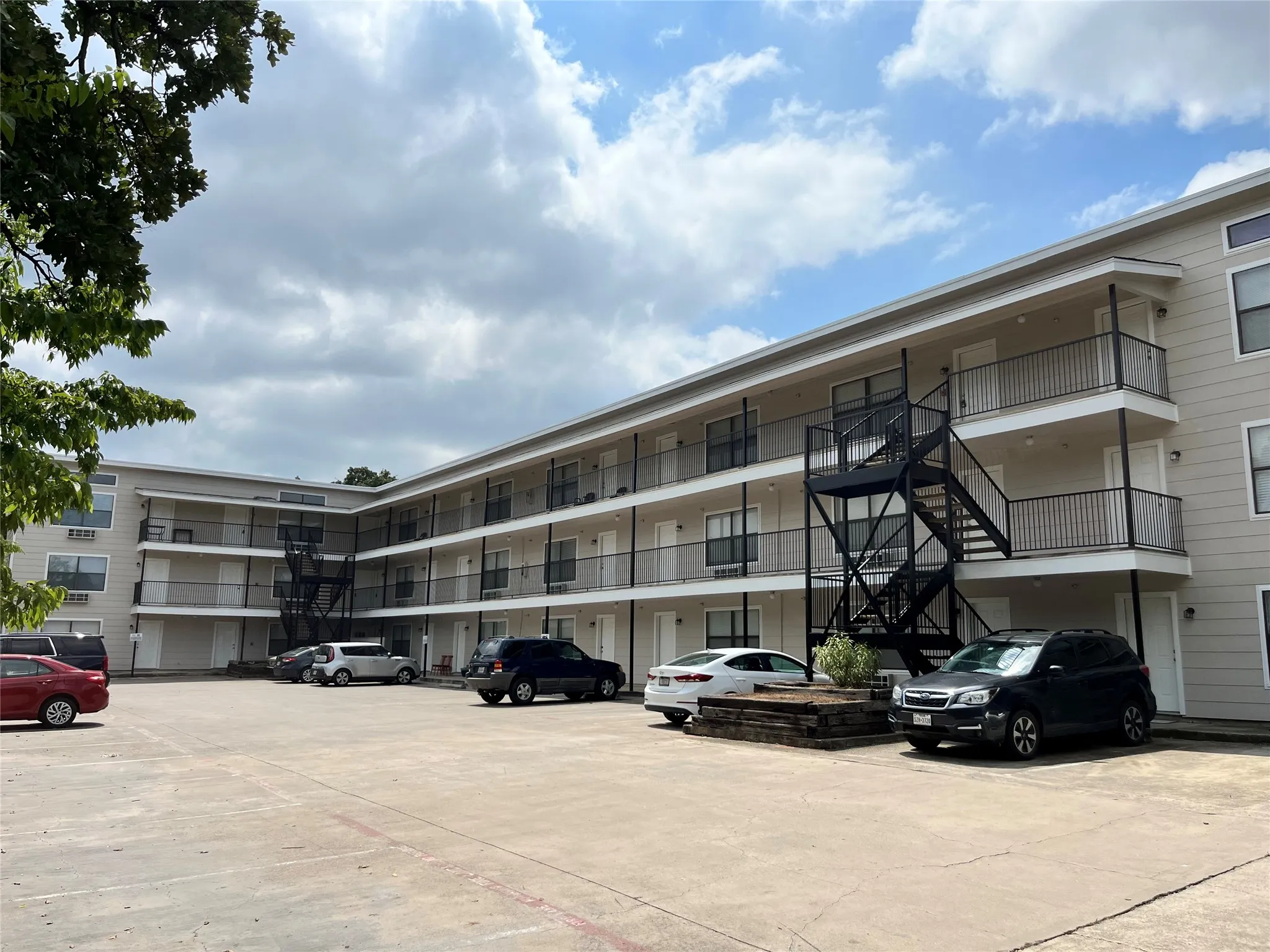 Exterior view of the multi-level residential complex with paved resident parking and clear blue skies.
