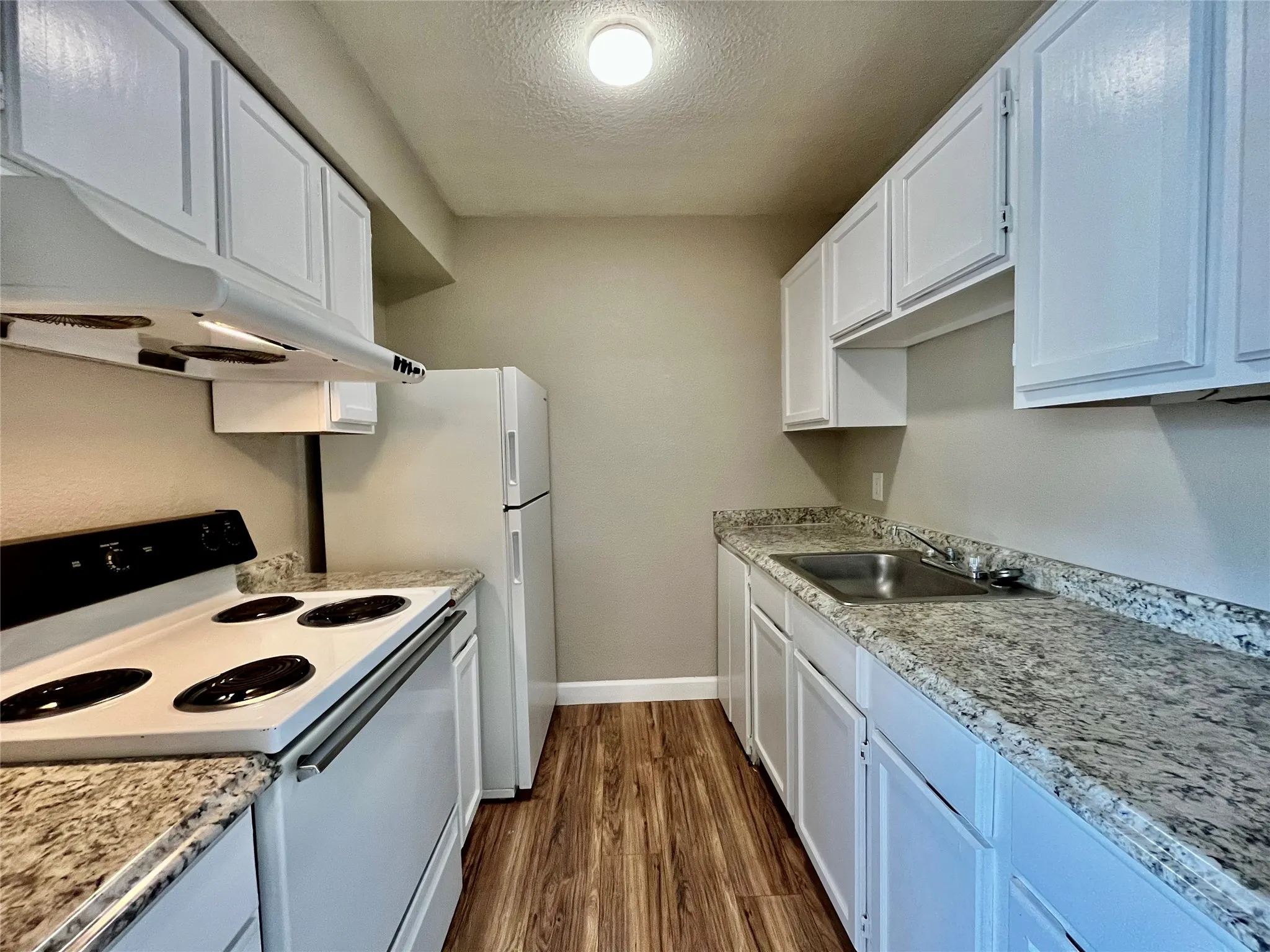 Functional galley-style kitchen equipped with white cabinetry, electric range, and clean finishes.