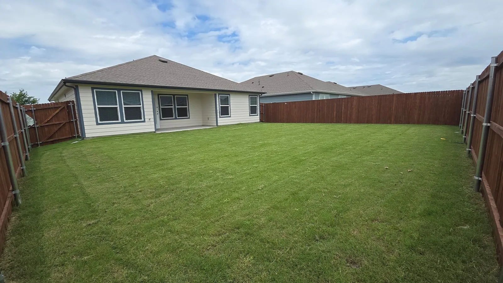 Expansive backyard featuring a manicured lawn, complete privacy fencing, and a concrete patio