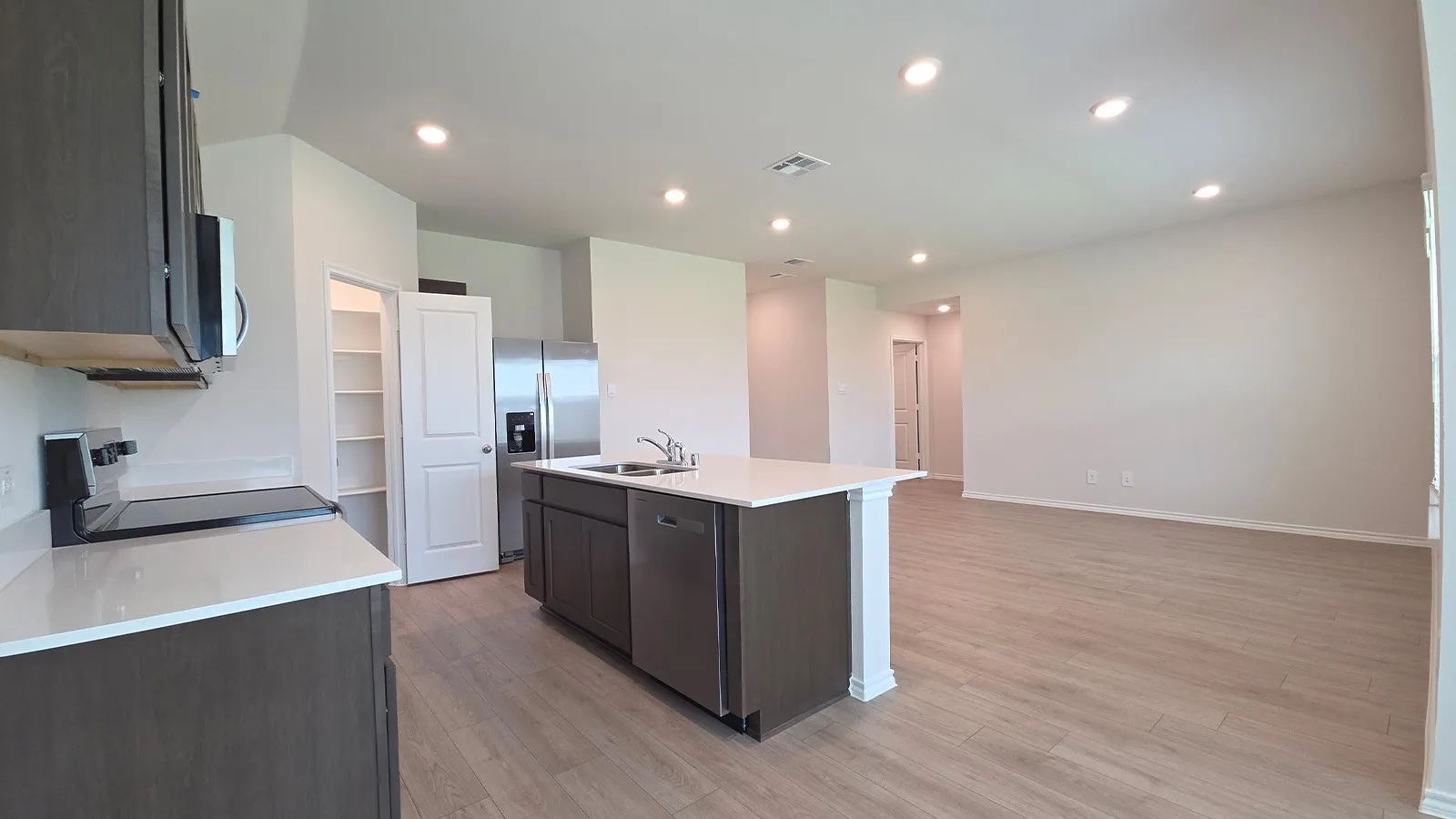 Open-concept kitchen and living area featuring wood-finish flooring throughout, recessed lighting, and a kitchen island with integrated sink and dishwasher